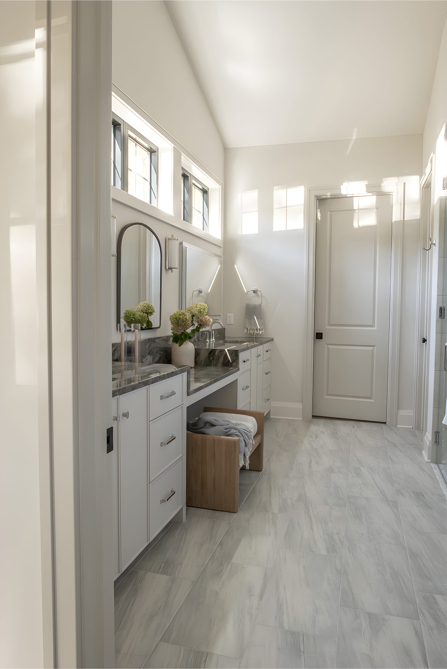 Spacious bathroom with tall mirrors, marble counters, double sinks, and bright natural light from high windows.