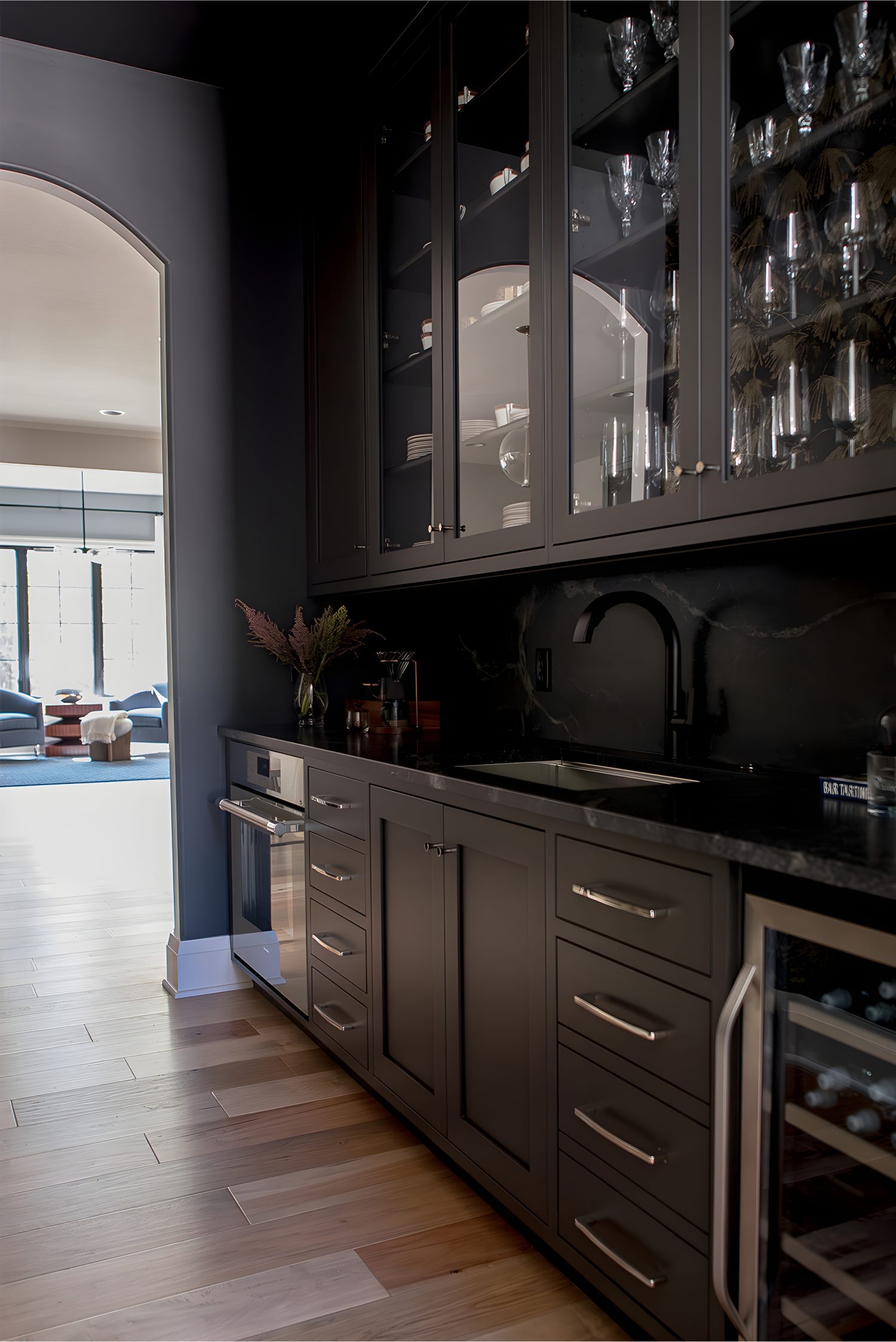 Sleek black cabinetry with glass doors and bar sink area featuring glassware display and dark marble backsplash