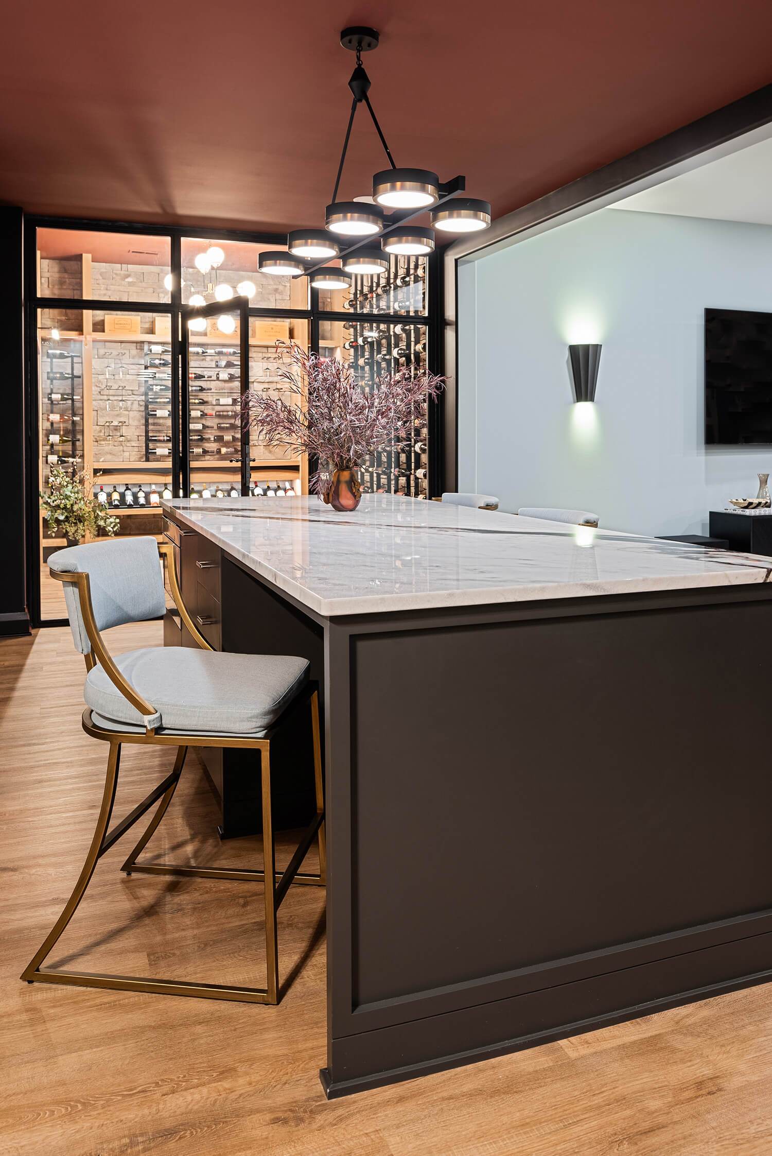 Modern kitchen island with marble top, sleek barstools, pendant lights, and glass wine cellar in warm contemporary design