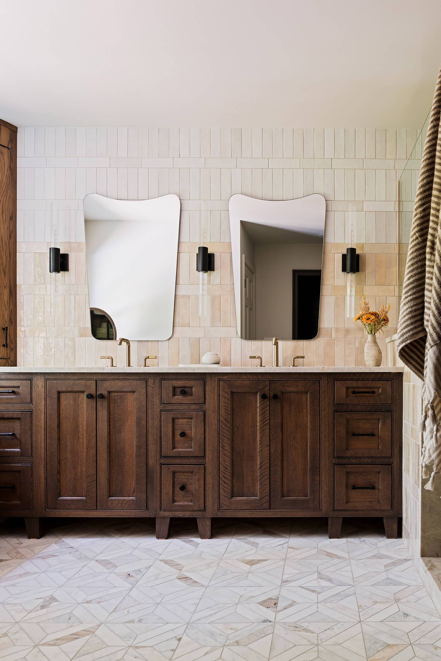Double sink vanity with dark wood cabinets, gold faucets, and two modern mirrors above.