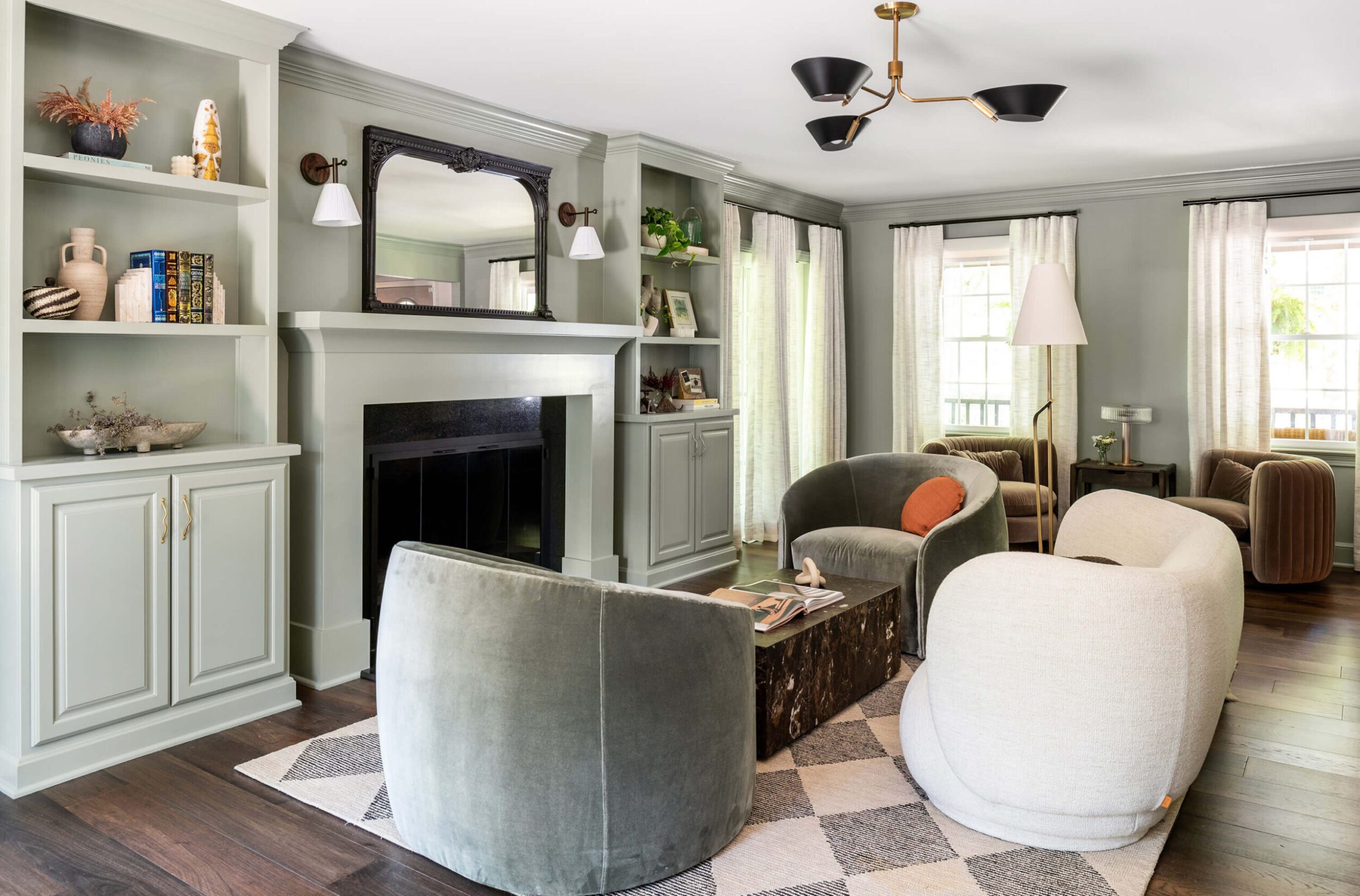 Spacious modern living room featuring sage cabinetry, round swivel chairs, fireplace, and layered textures with neutral tones.