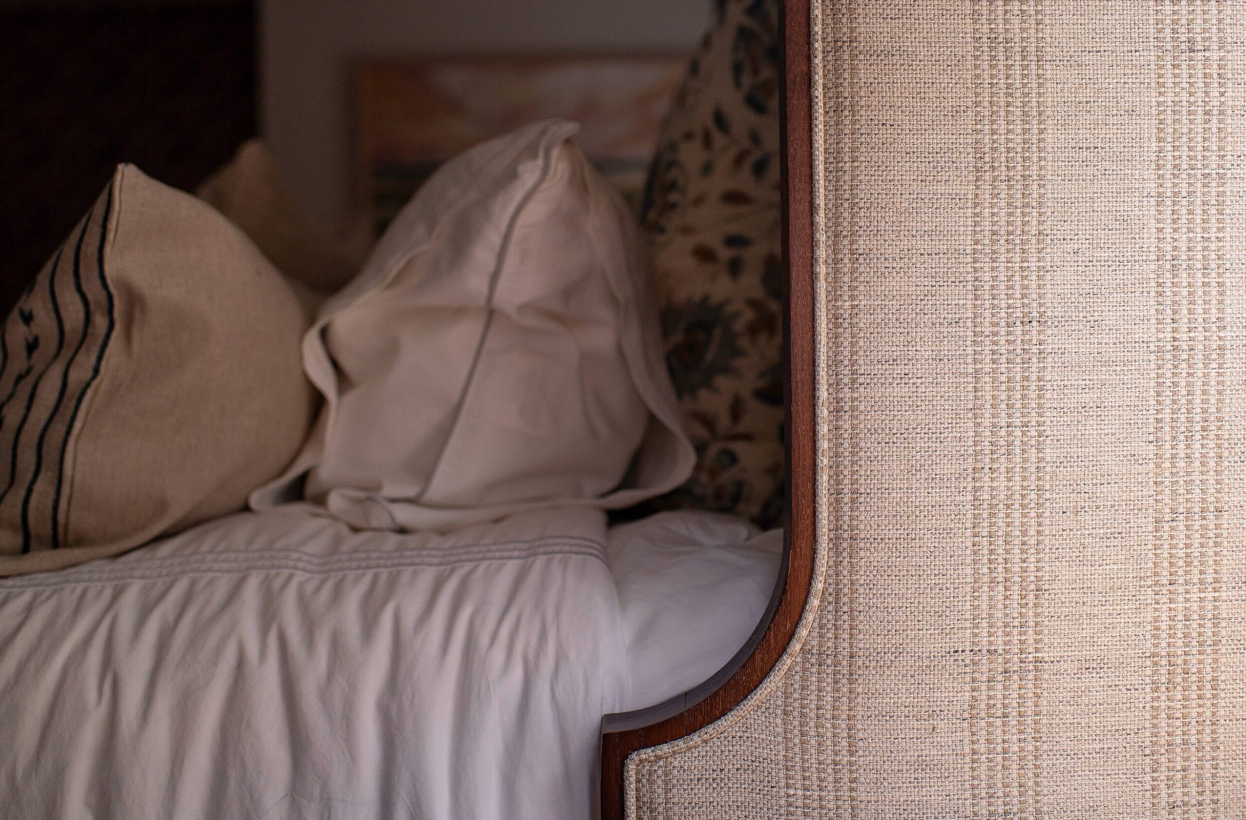 Close-up of textured headboard and neutral striped pillows with cozy layered bedding, creating a soft and inviting look.