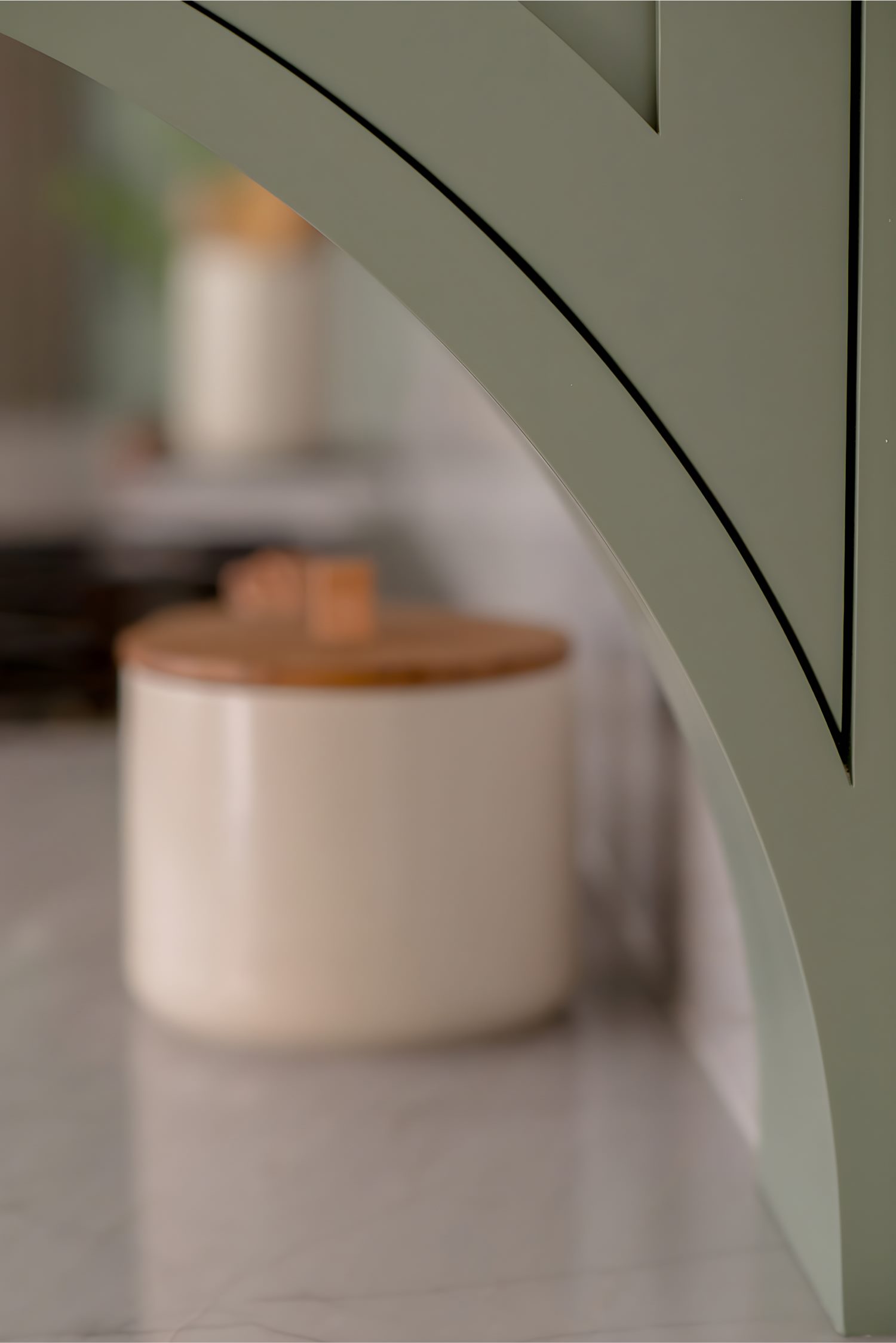 Close-up of curved green arch detail framing blurred round container with wooden lid on marble countertop background