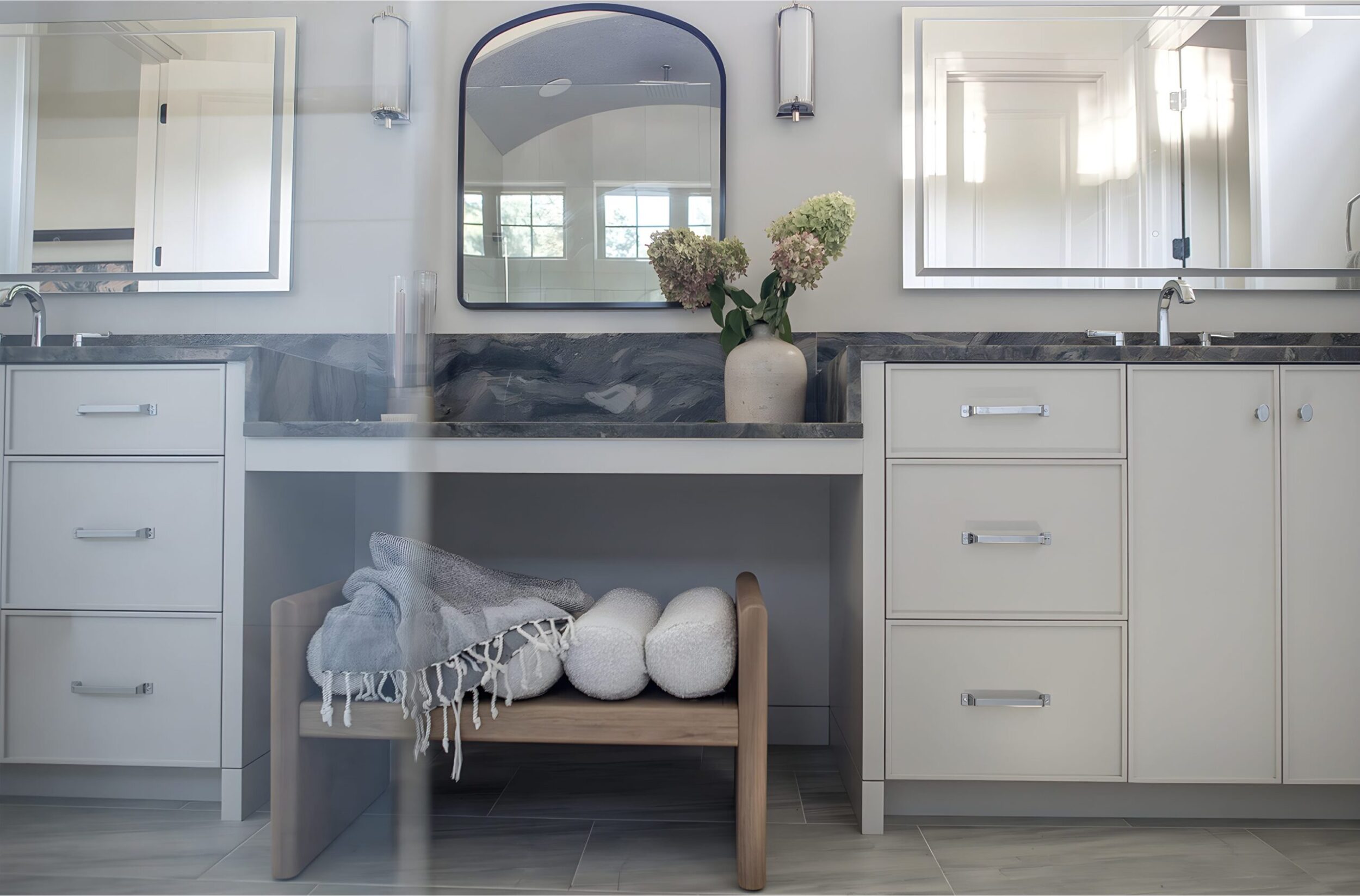 Contemporary double vanity with marble counters, mirrors, and decorative vase, styled with folded towels and bench.