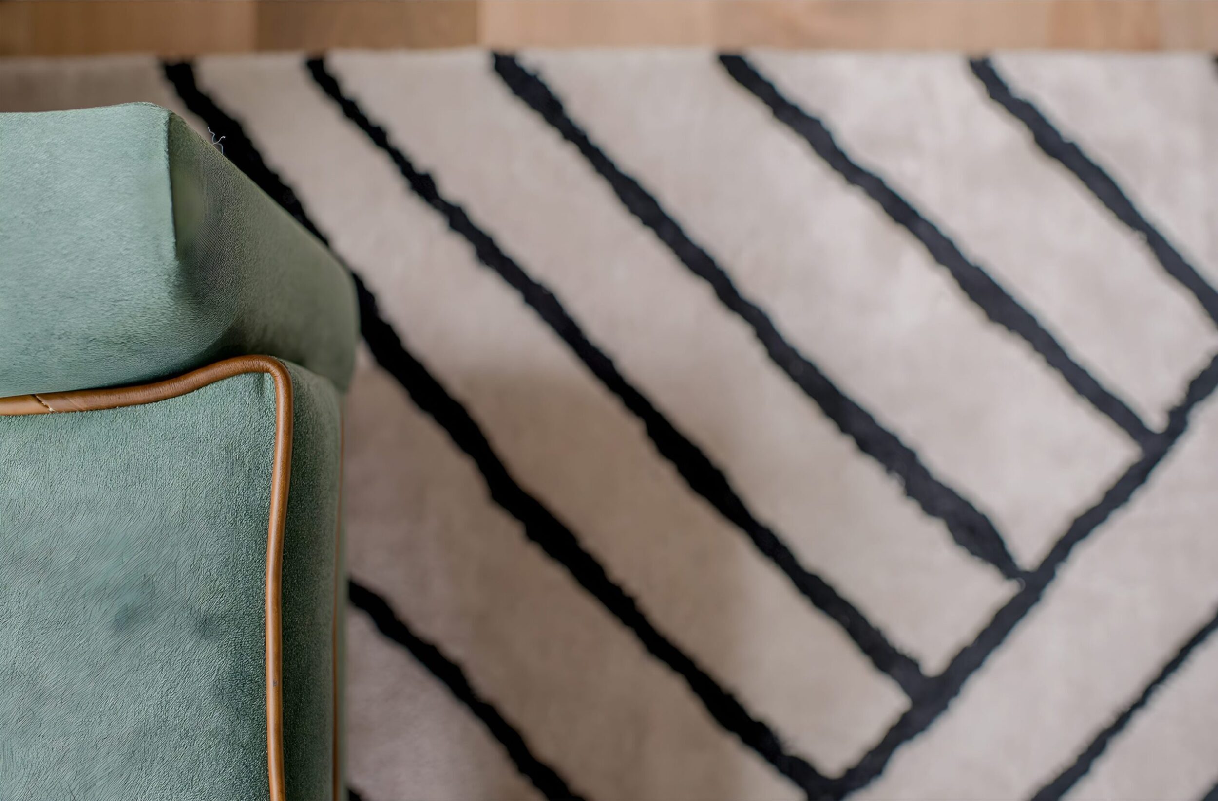 Close-up of mint green chair corner with tan trim, set against a cream rug with bold black diagonal stripes