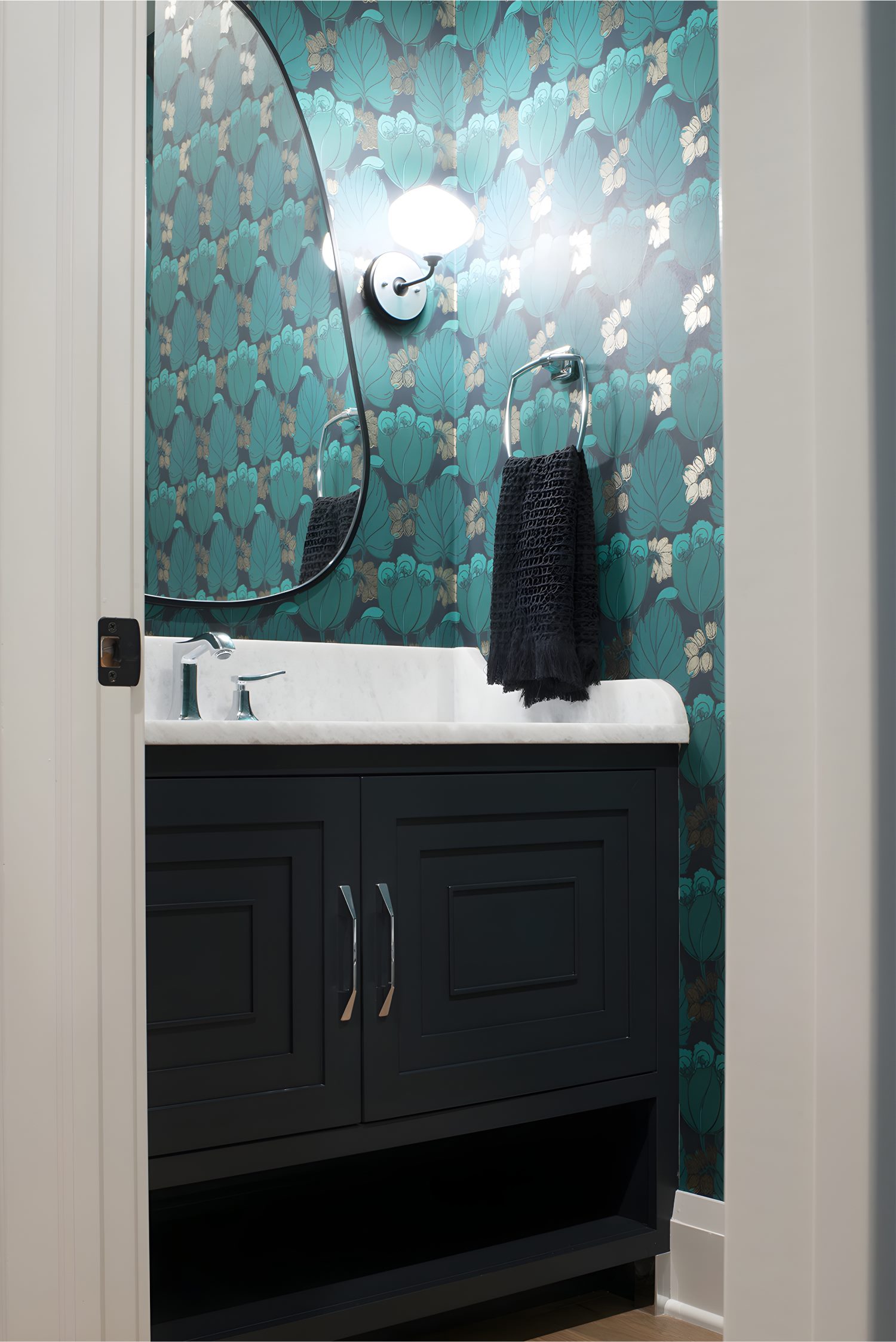 Bold powder room with teal floral wallpaper, unique curved mirror, dark vanity cabinet, and marble countertop