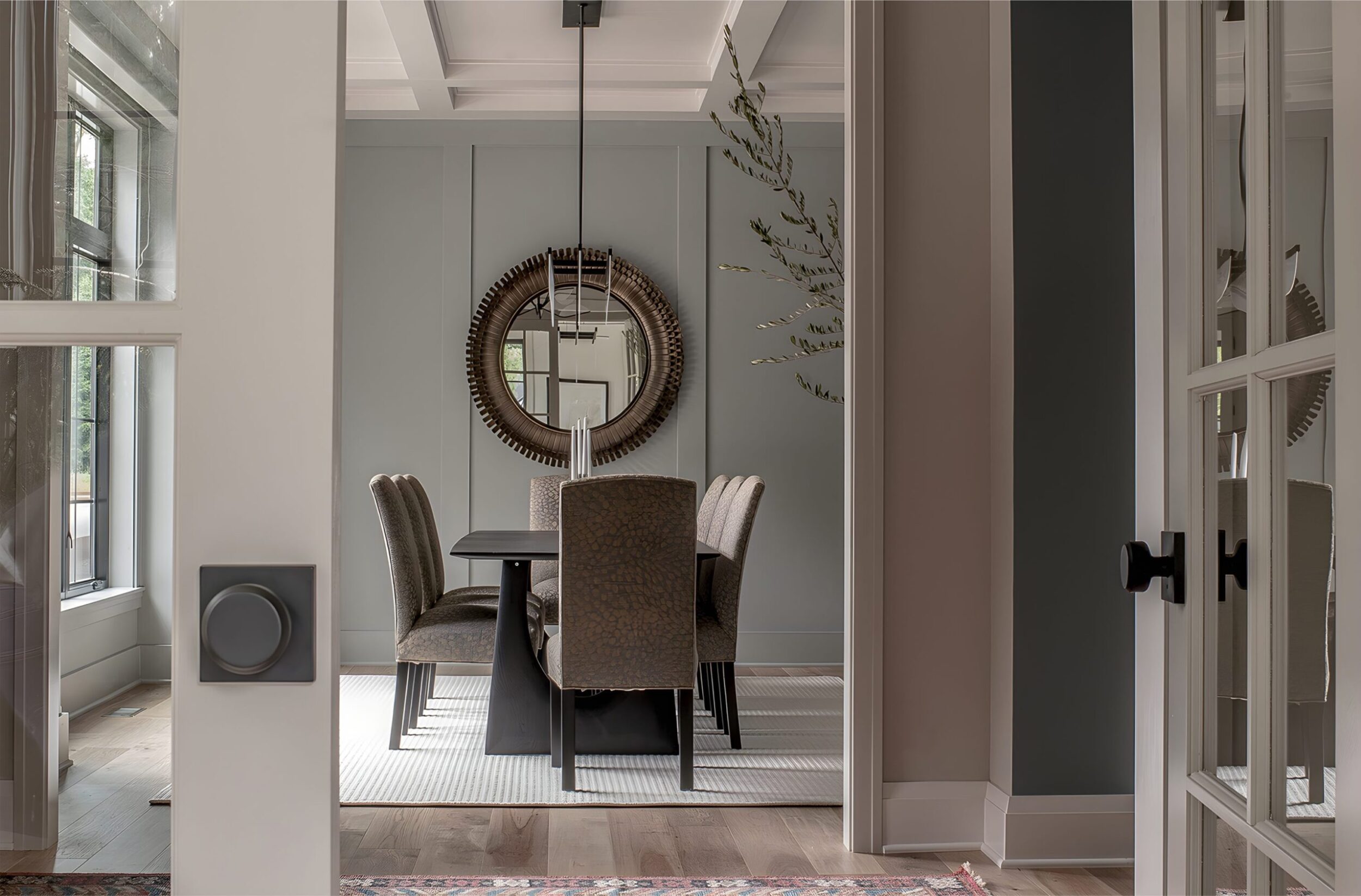 Dining room with round mirror, black dining table, upholstered chairs, pendant light, and wall paneling