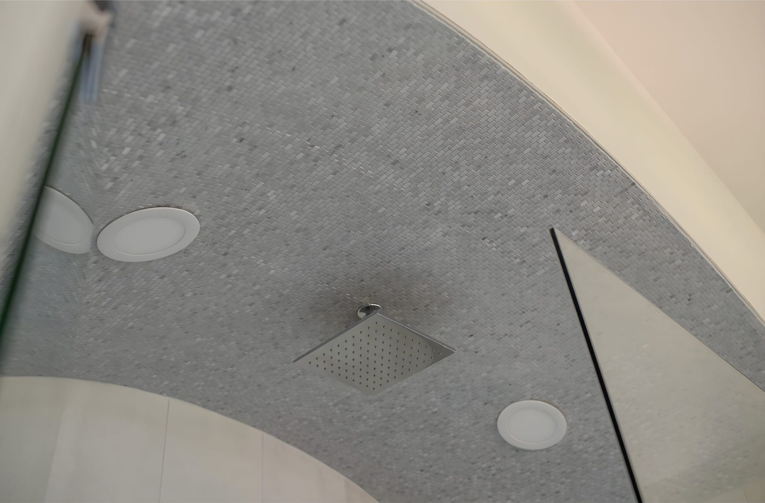 Modern shower ceiling with mosaic tile, recessed lighting, and square rainfall showerhead in minimalist bathroom.