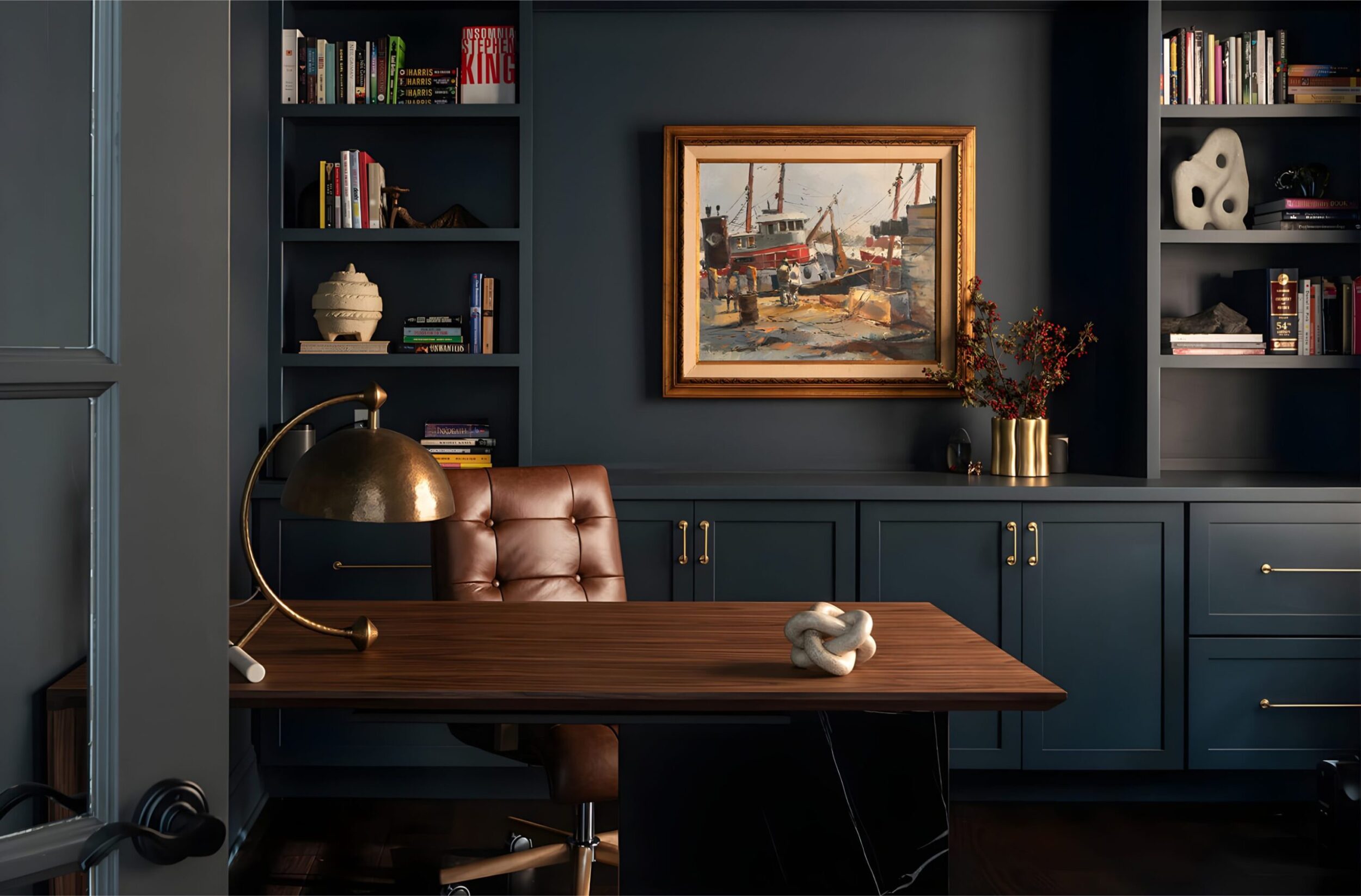 Elegant home office with blue built-in shelves, brown leather chair, wooden desk, gold lamp, and framed painting