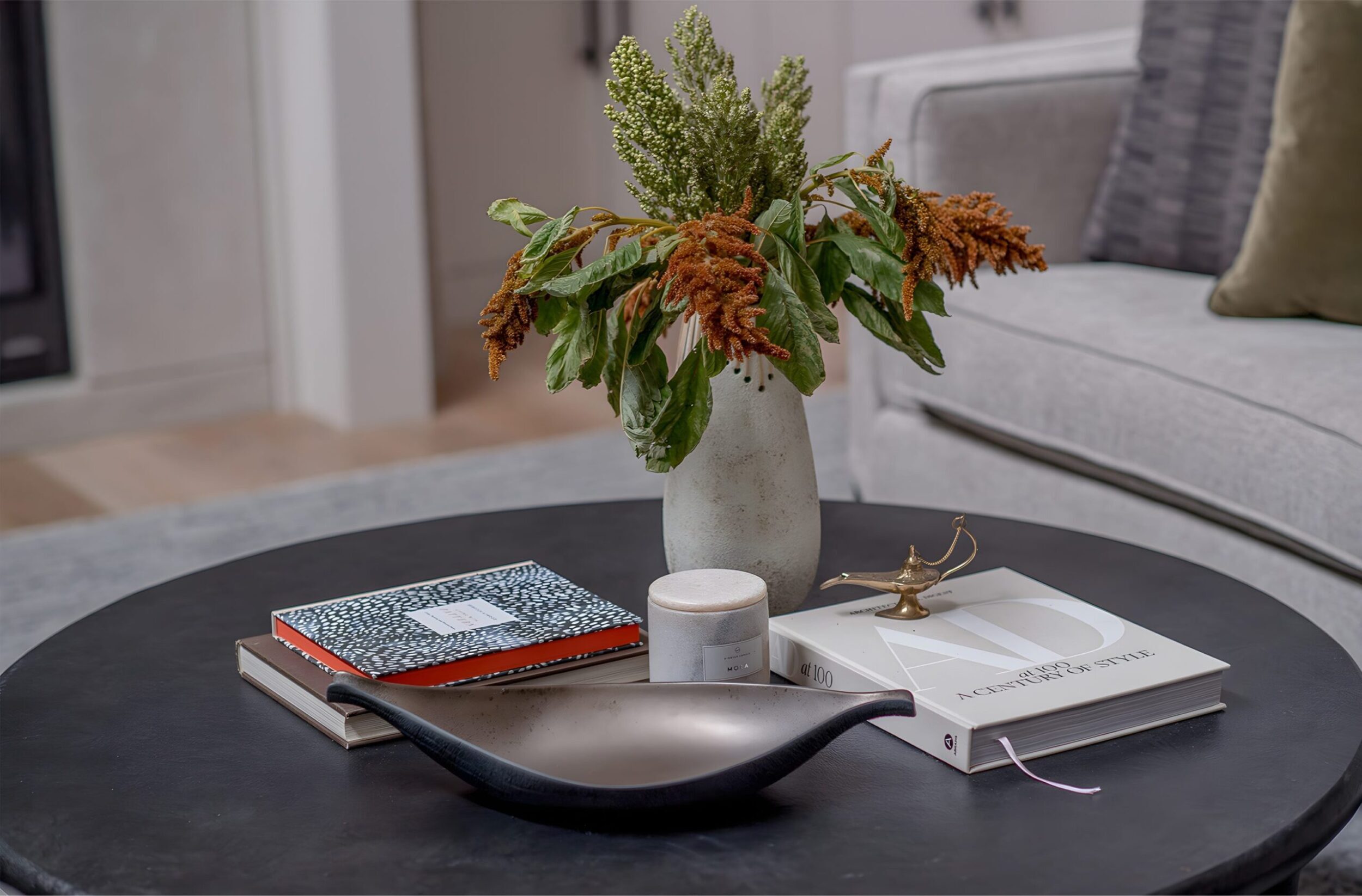 Black round coffee table with vase, books, candle, and decorative tray