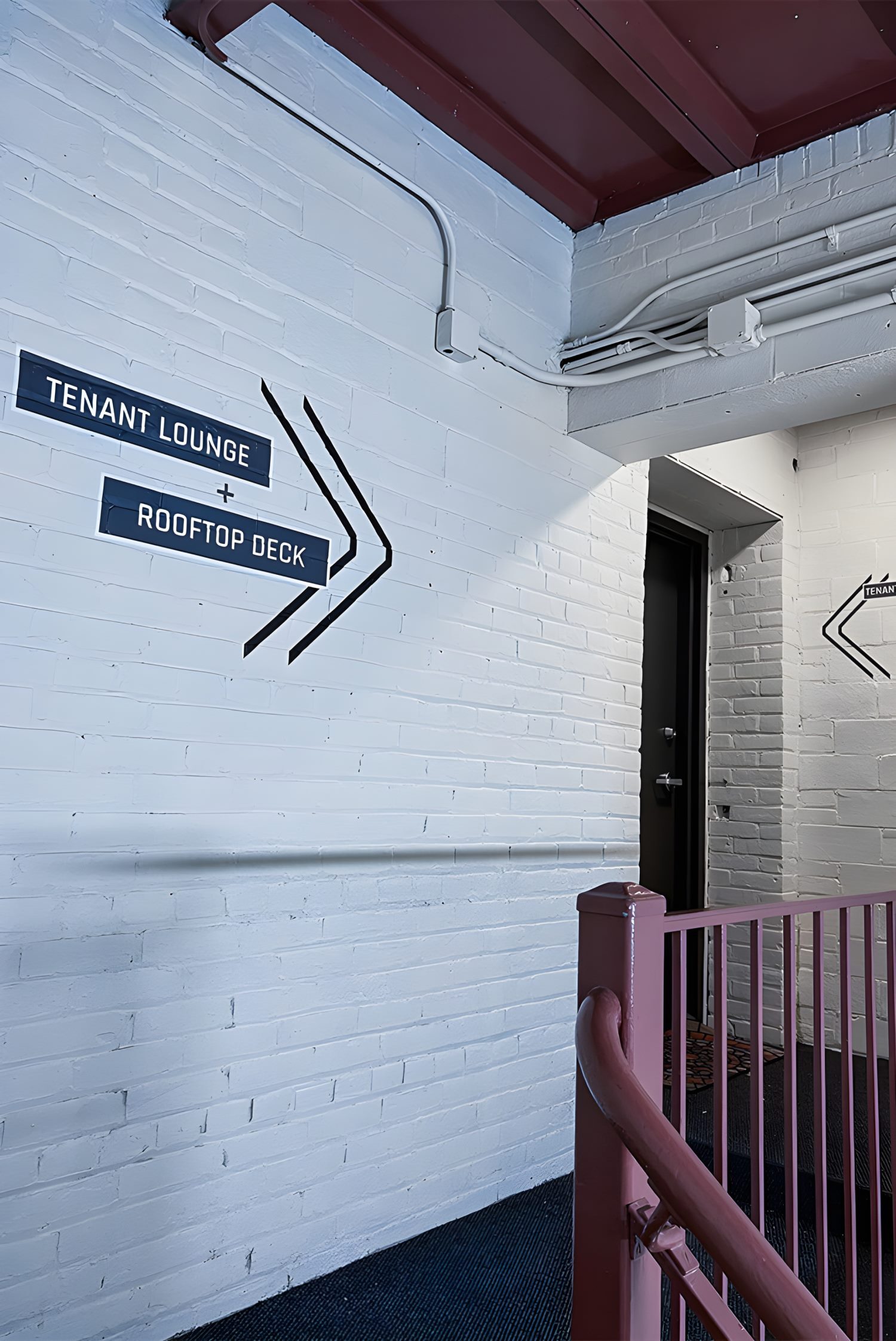 White brick stairwell with black signage pointing toward tenant lounge and rooftop deck.