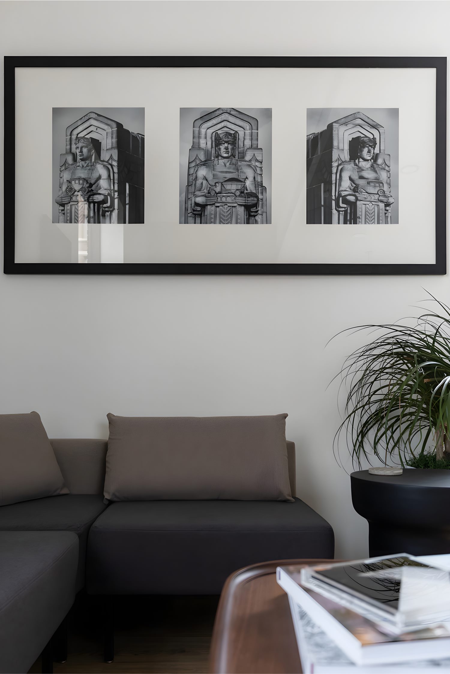 Black-and-white triptych artwork of architectural statues above sectional sofa with potted plant nearby.