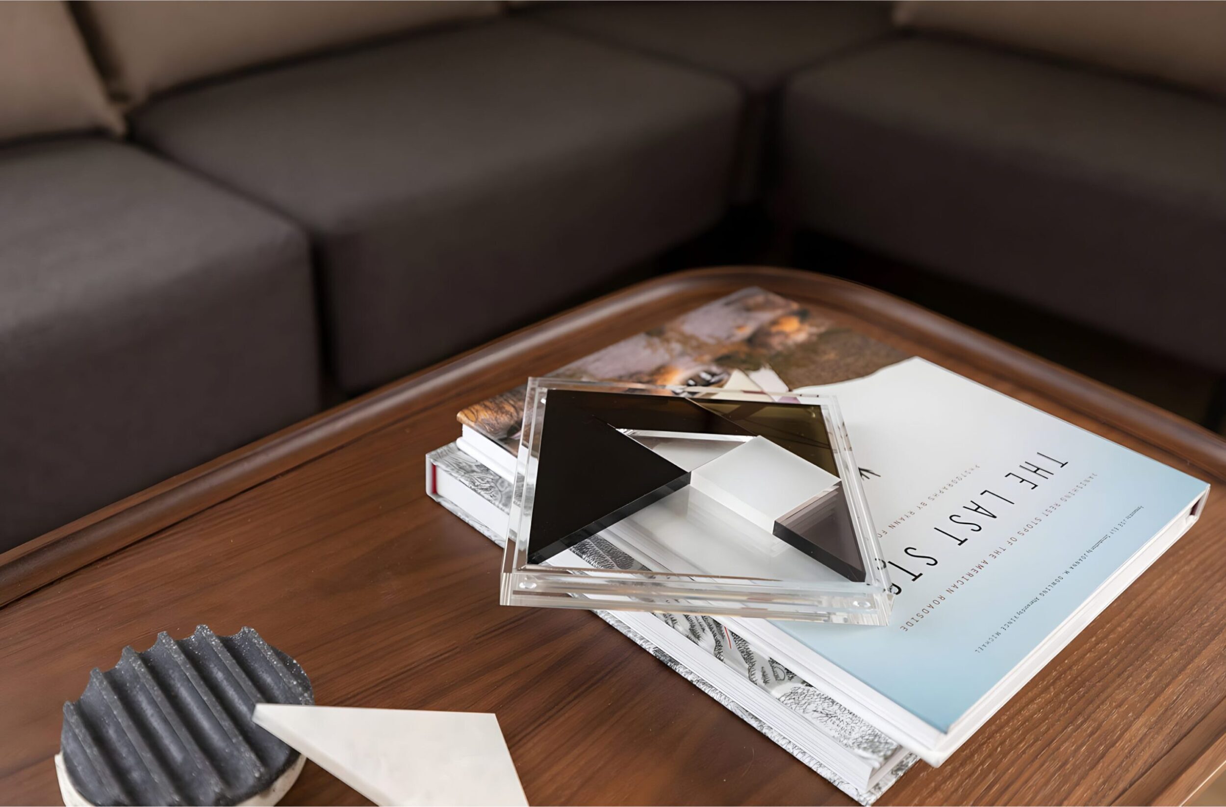 Close-up of lounge coffee table with stacked books, geometric decor, and cushioned sofa seating.