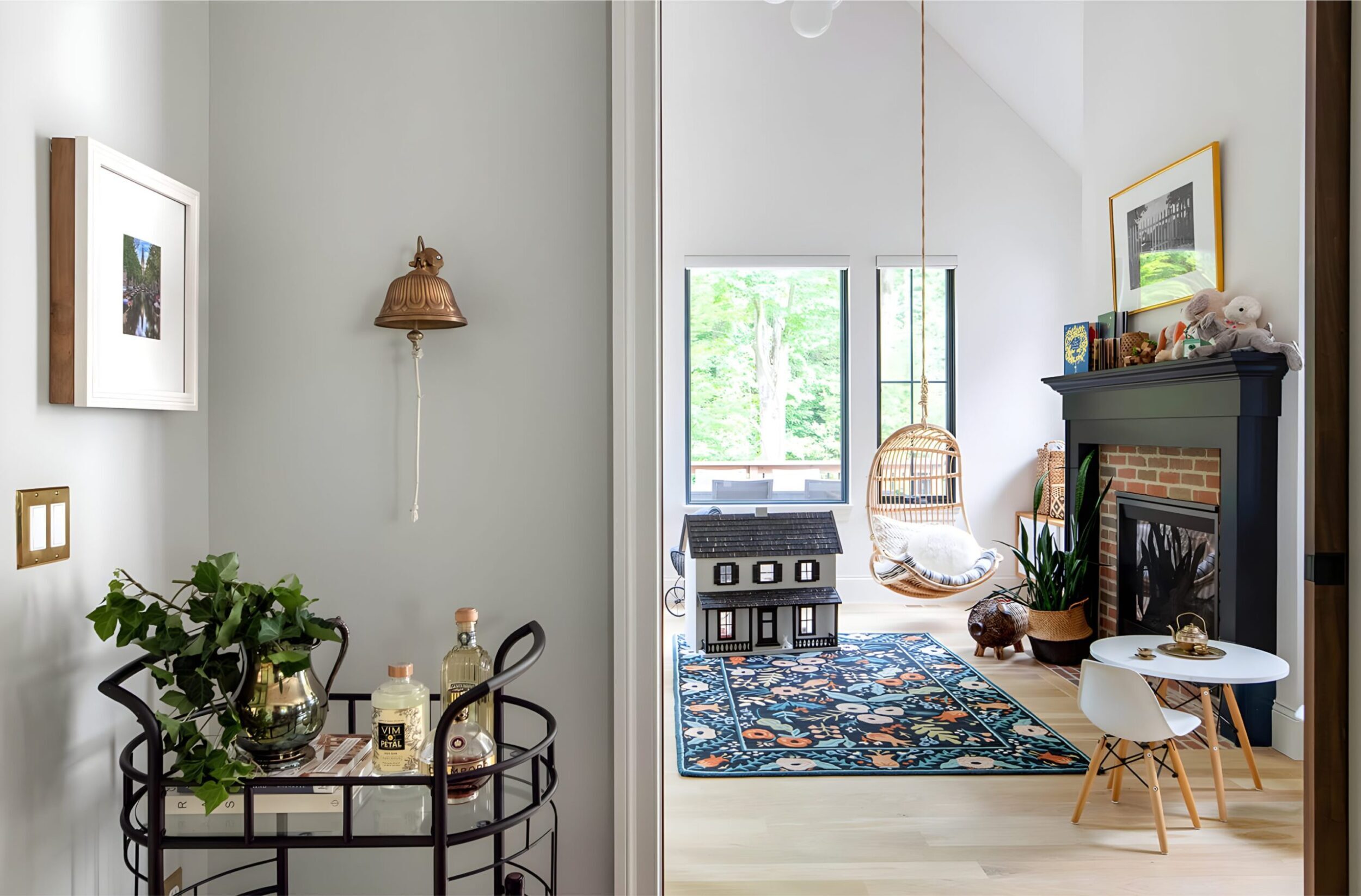 Bright hallway view into playful room with dollhouse, hanging chair, bar cart, and brick fireplace.
