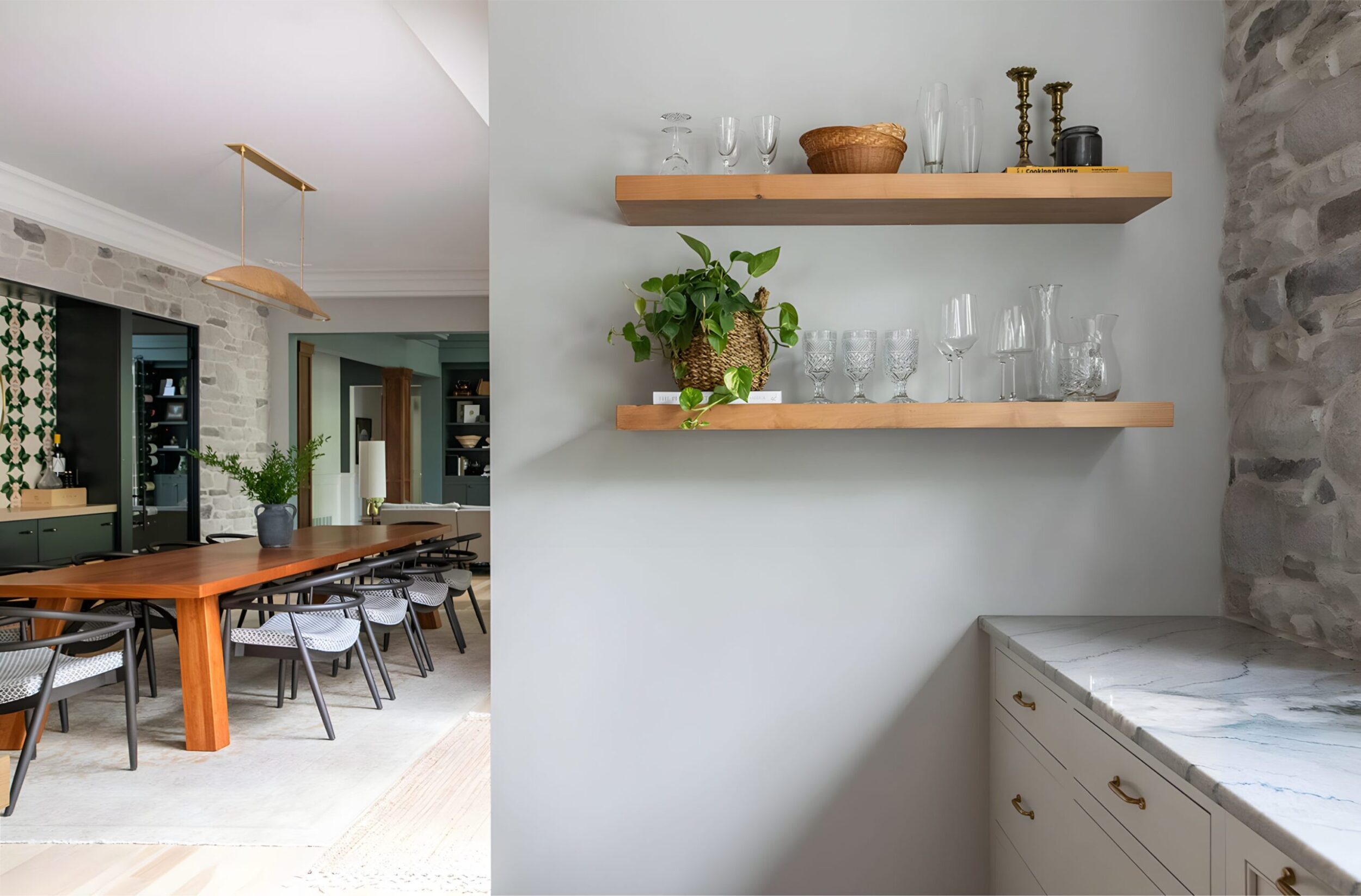 Floating wood shelves with glassware, woven basket, and potted plant, overlooking dining room with long wood table.