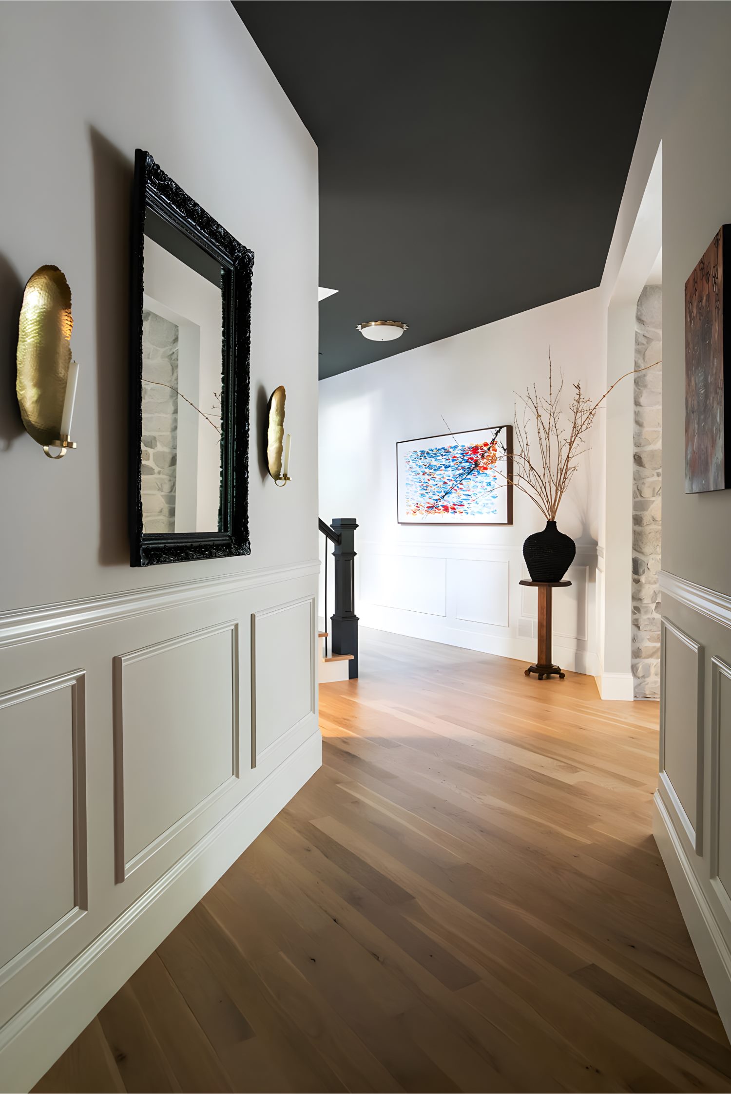 Hallway with wood flooring, dark ceiling, black framed mirror, and artwork leading toward staircase.