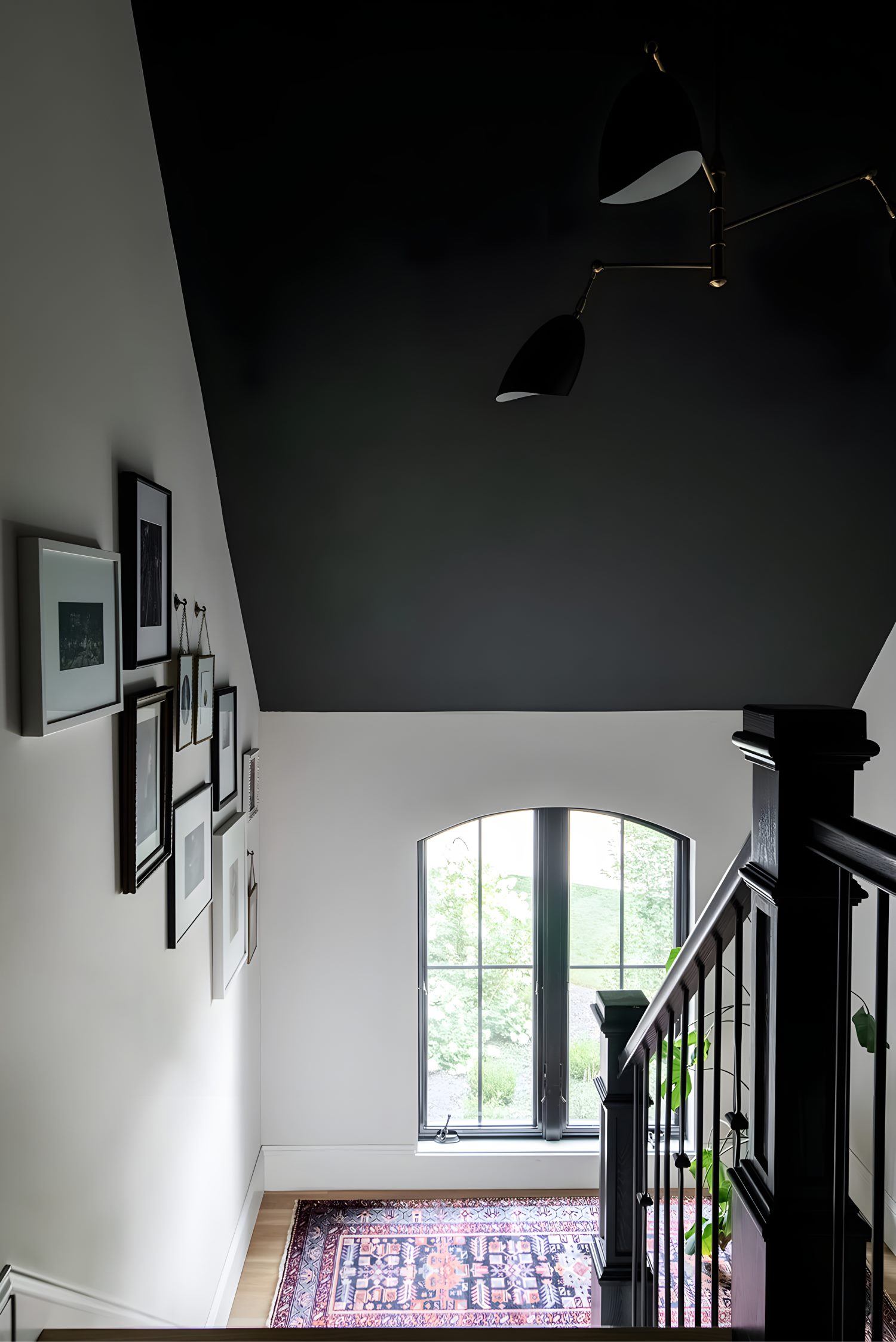 Stairwell with gallery wall, black ceiling, large window, and patterned rug adding contrast and warmth.