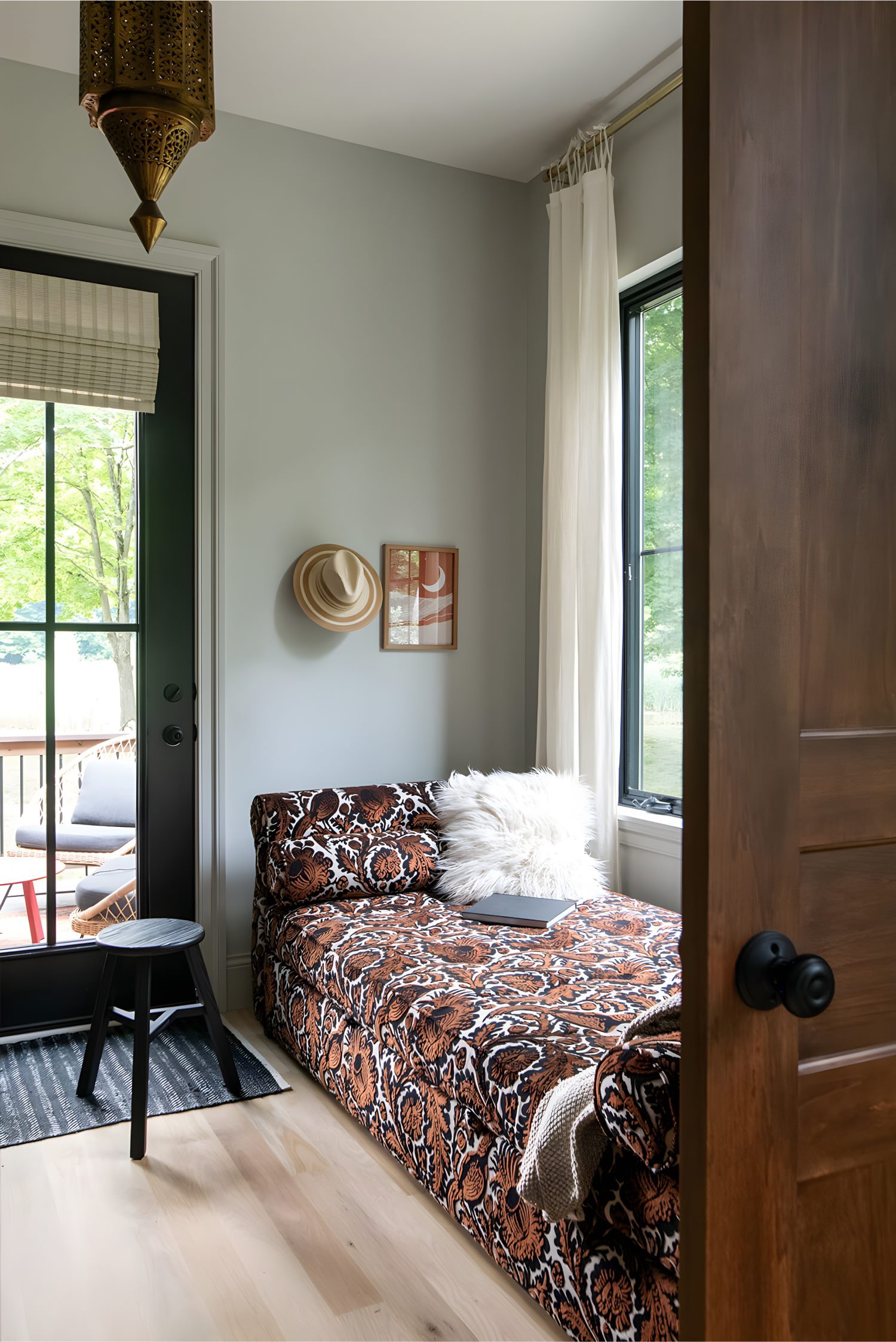 Cozy nook with patterned daybed, fluffy pillow, wall art, and glass door opening to outdoor seating.
