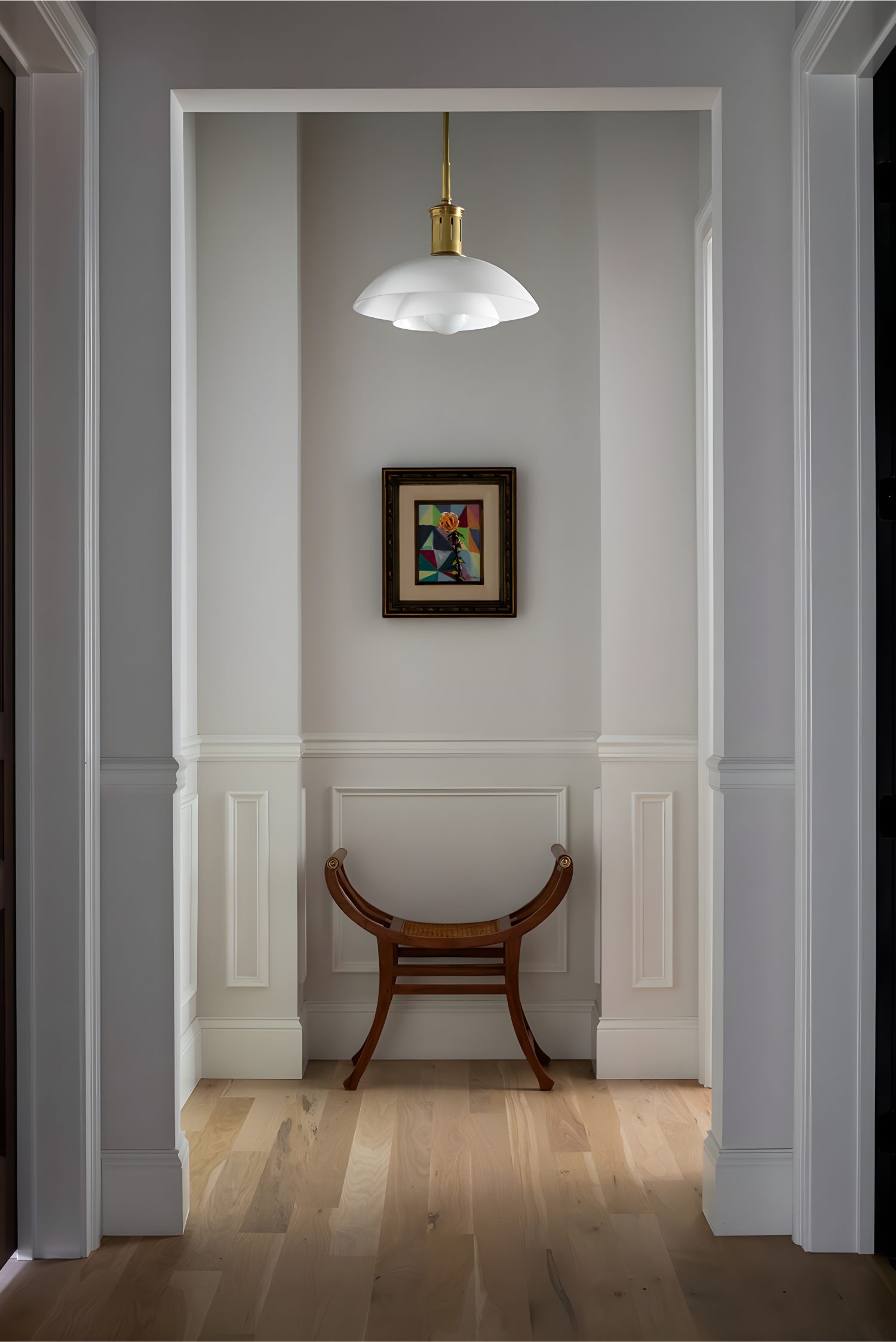 Narrow hallway with white wainscoting, chair, framed art, and pendant light