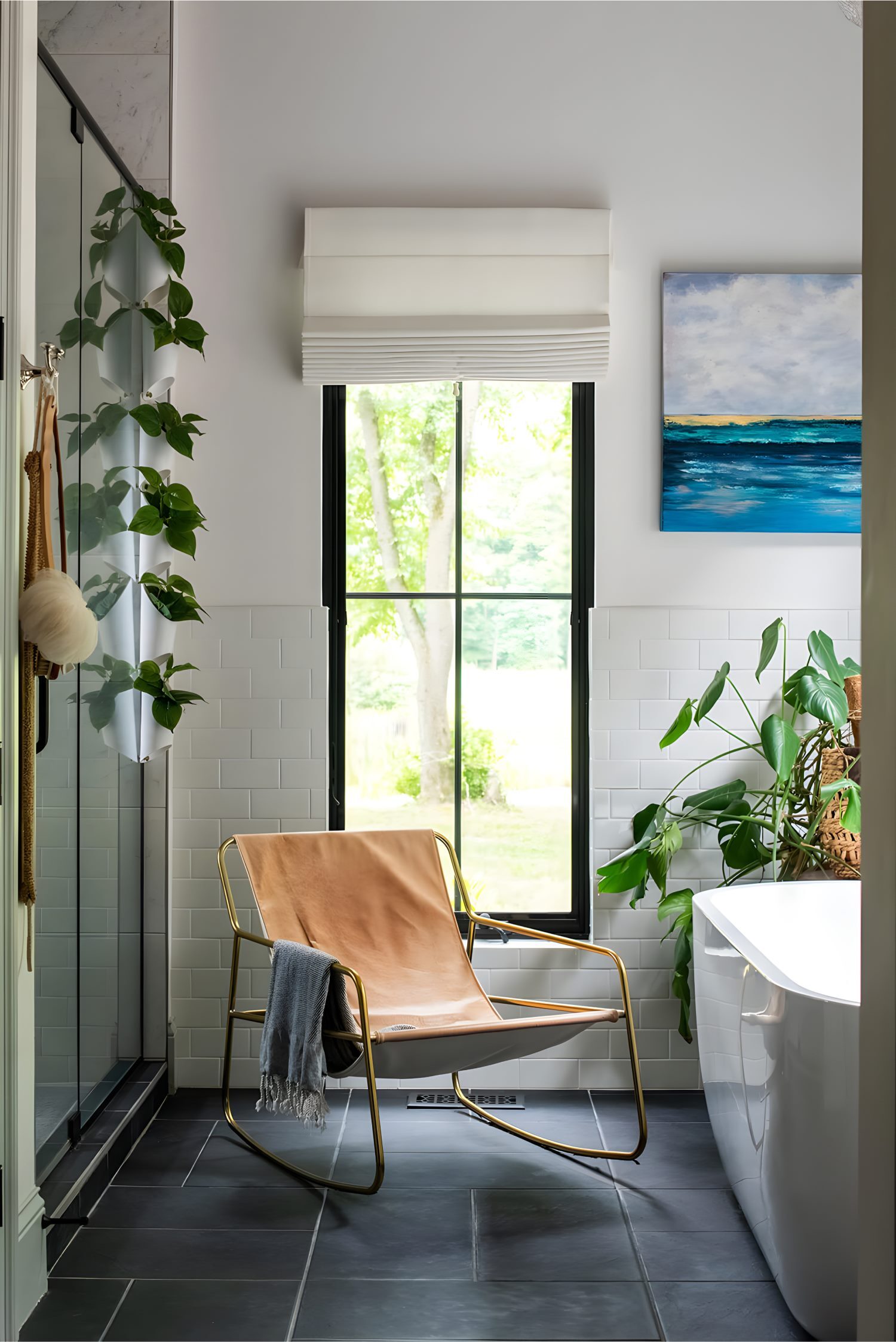 Bright bathroom with window, leather sling chair, plants, glass shower, and ocean artwork on wall.