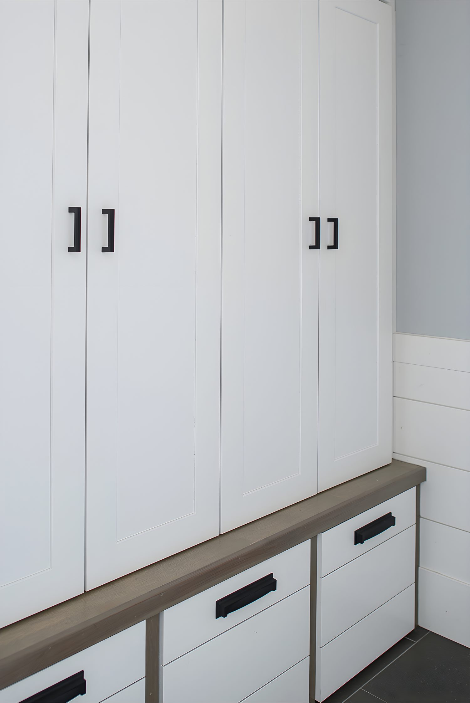 White mudroom cabinetry with black handles, showing open drawer on casters for hidden storage in tiled hallway.