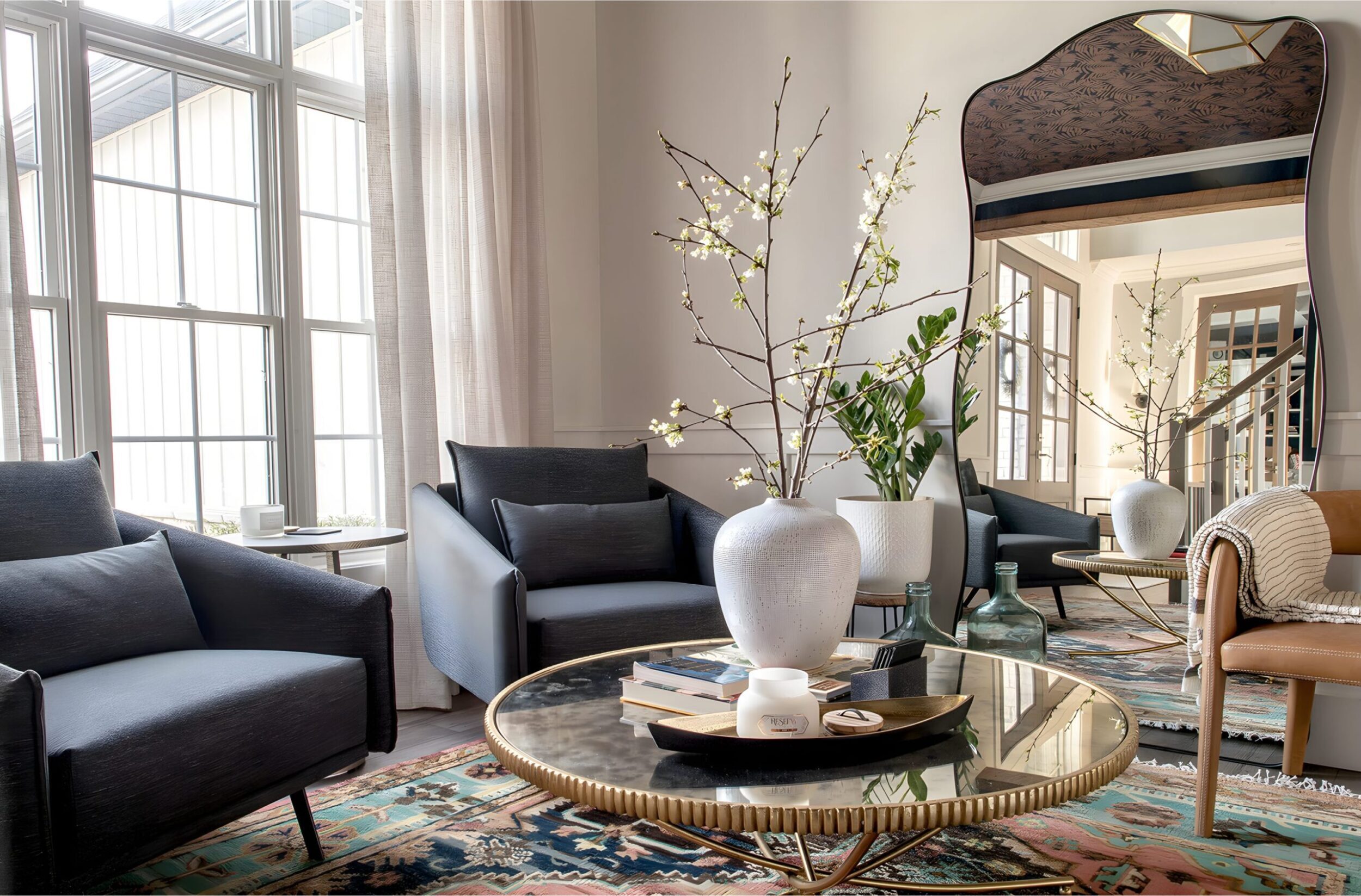Living room with large windows, patterned rug, modern chairs, and floral arrangements styled by interior decorator.
