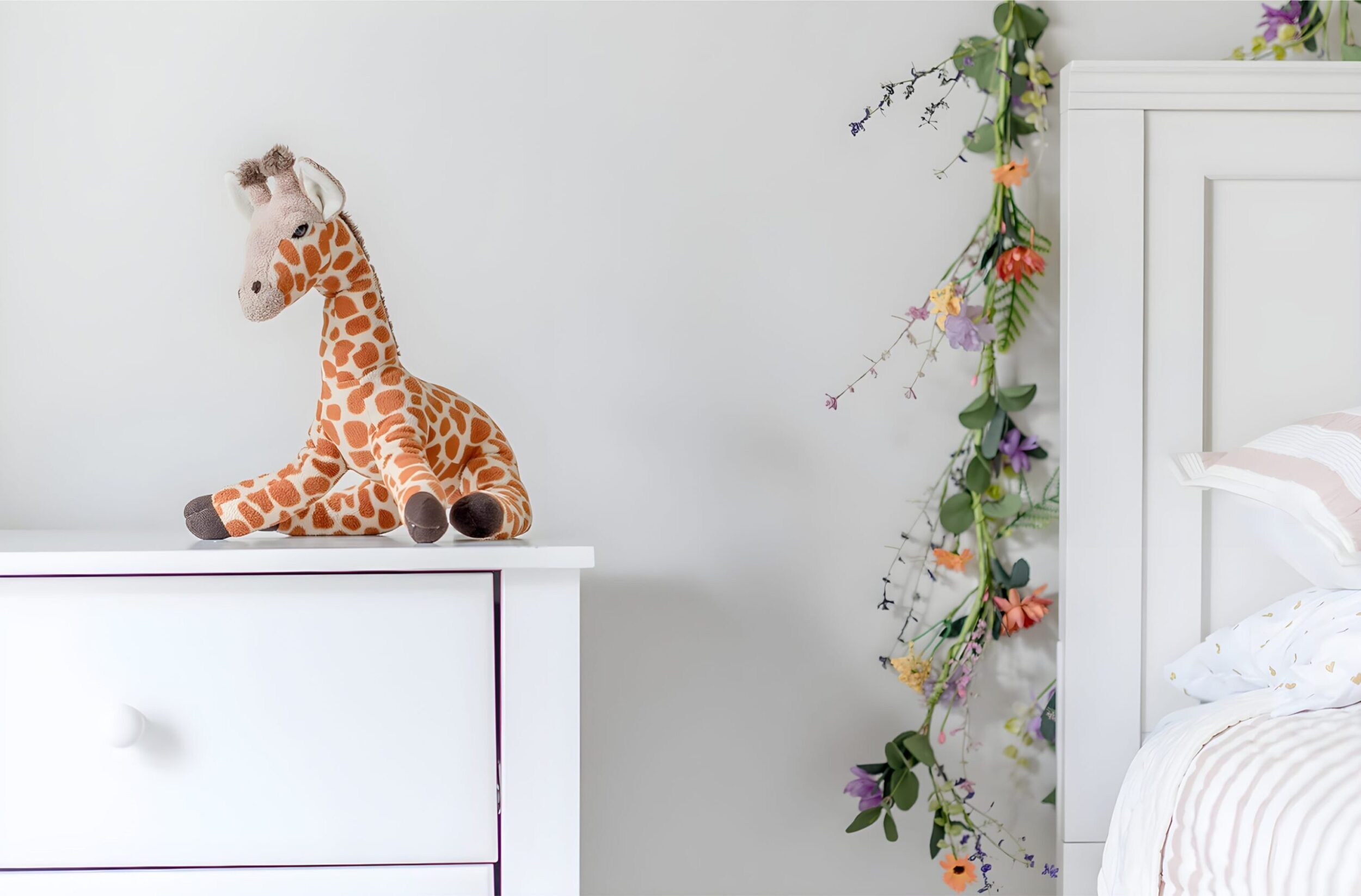 Bright children’s bedroom styled with white furniture, playful accents, floral garland, and cozy textiles