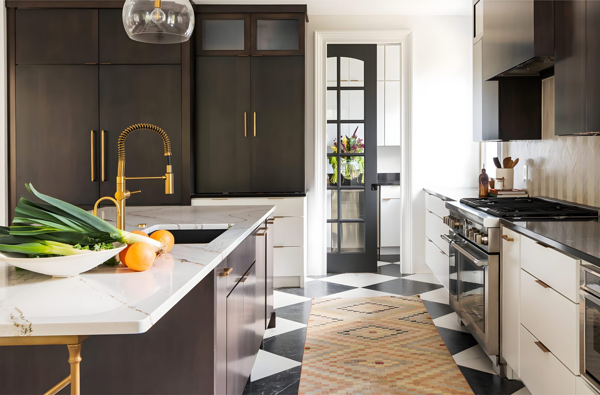 Contemporary kitchen with dark cabinets, brass fixtures, marble island, and checkered floor leading to glass door pantry