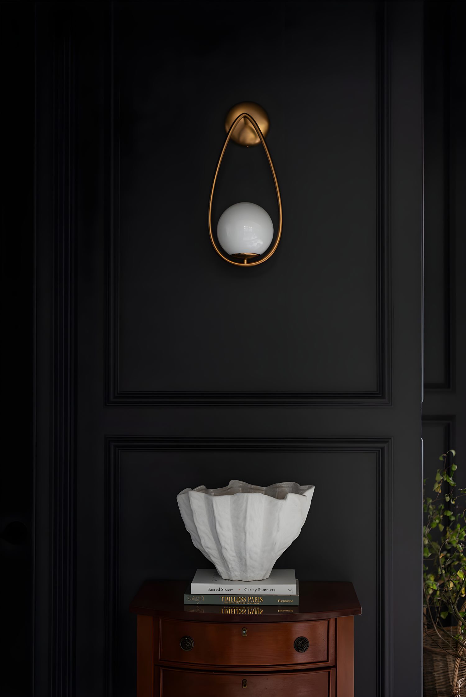 Gold wall sconce with round white bulb mounted on matte black paneled wall, styled above wood console and decorative accent