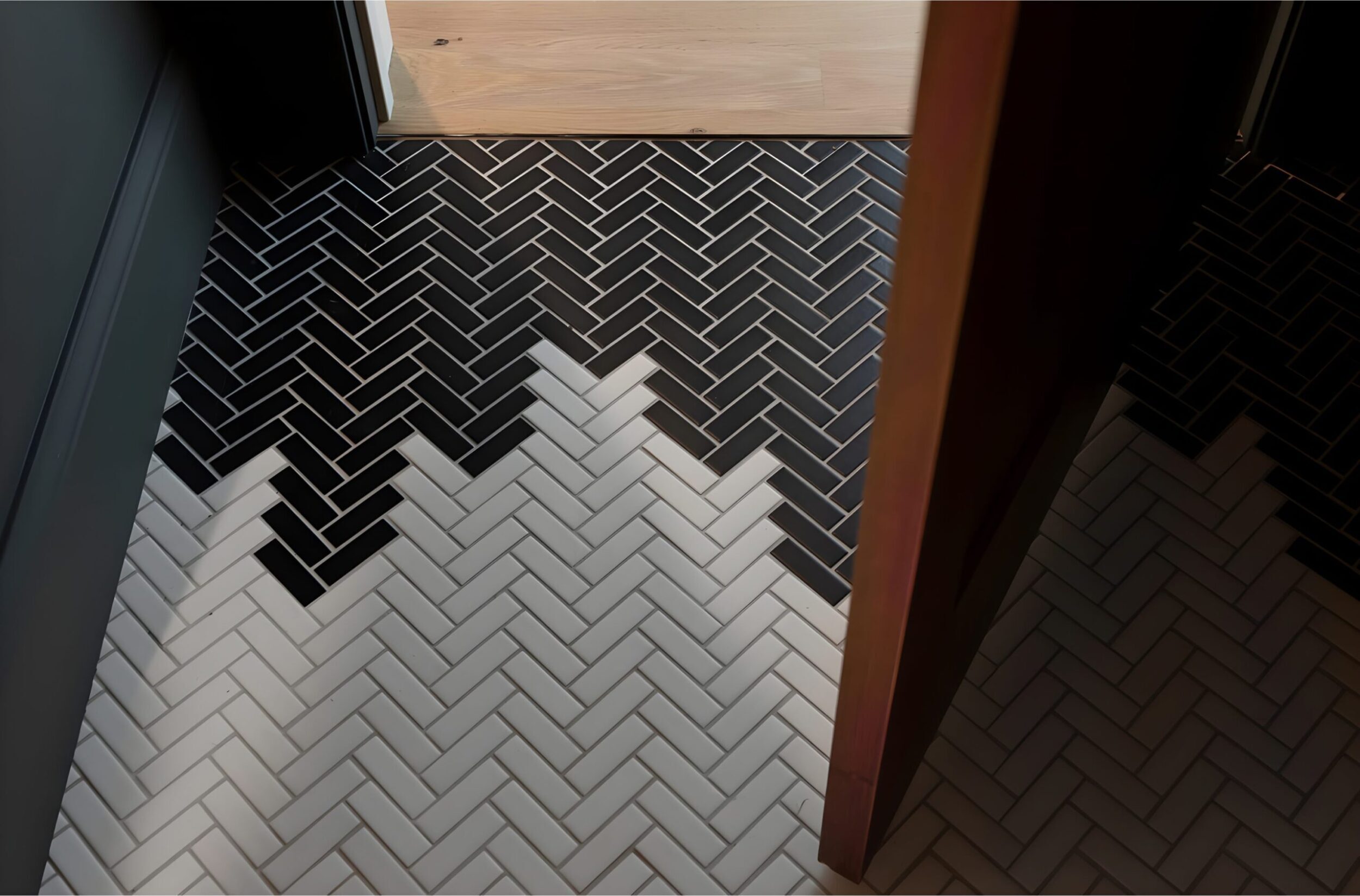 Black and white herringbone tile floor transitioning in bold geometric pattern from dark tones to light at doorway entrance