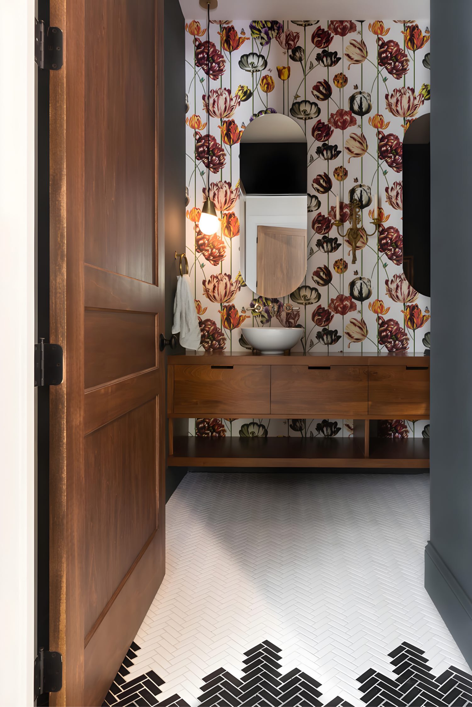 Chic powder room with patterned wallpaper, gold mirror, white sink, and wall-mounted brass light fixtures.