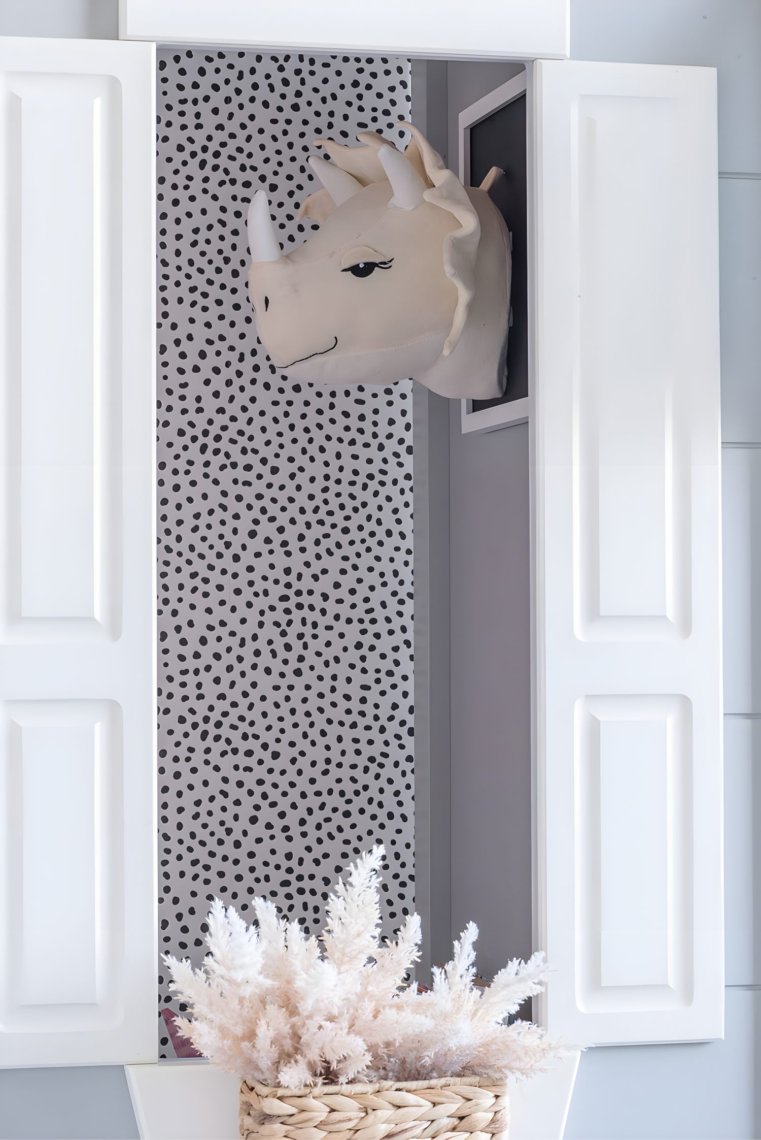 Kids’ bedroom detail with stuffed dinosaur wall mount, spotted wallpaper, and woven basket of white faux florals