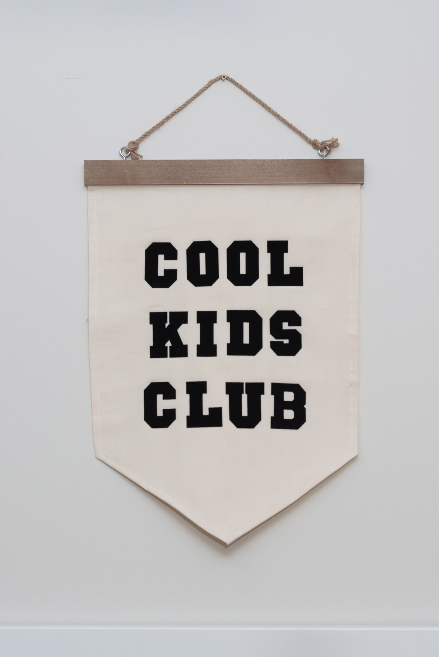 Canvas wall banner with bold black “COOL KIDS CLUB” lettering hanging on a plain white wall.