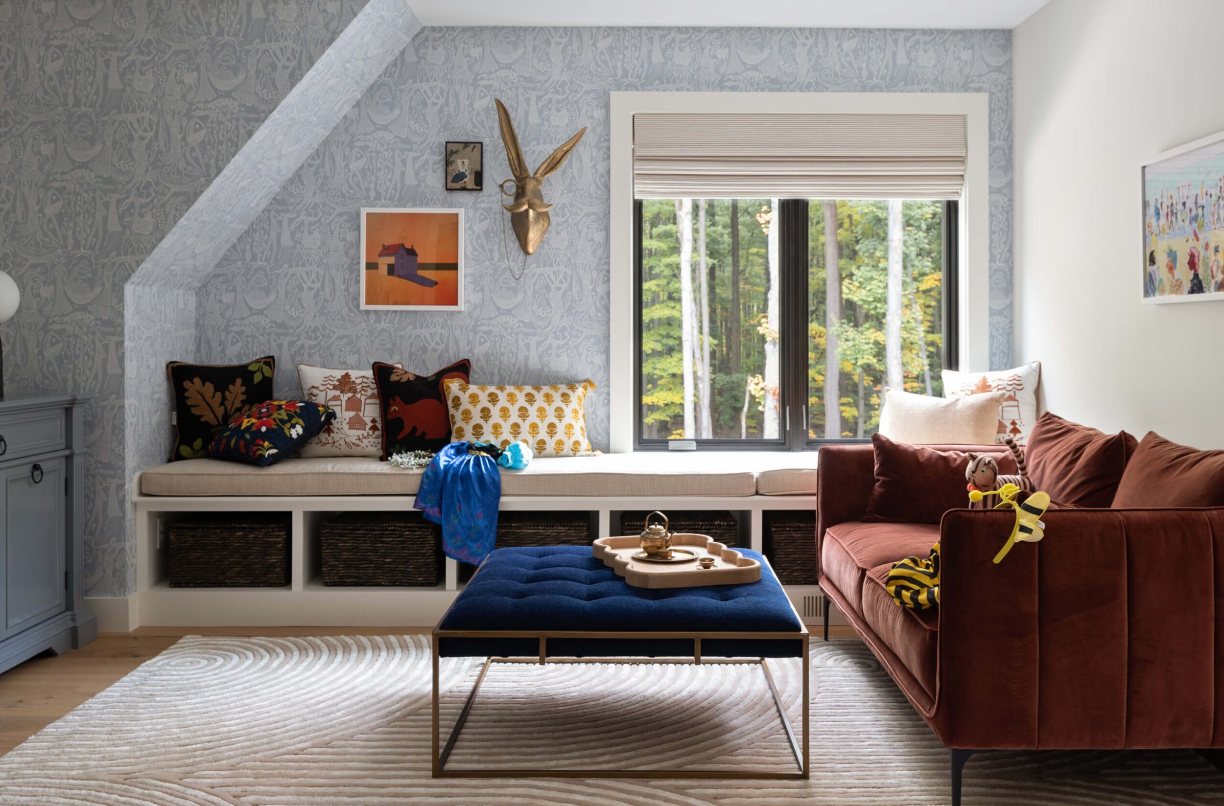 Kids’ lounge with patterned wallpaper, bench seating, colorful throw pillows, and plush sofa creating a playful space.
