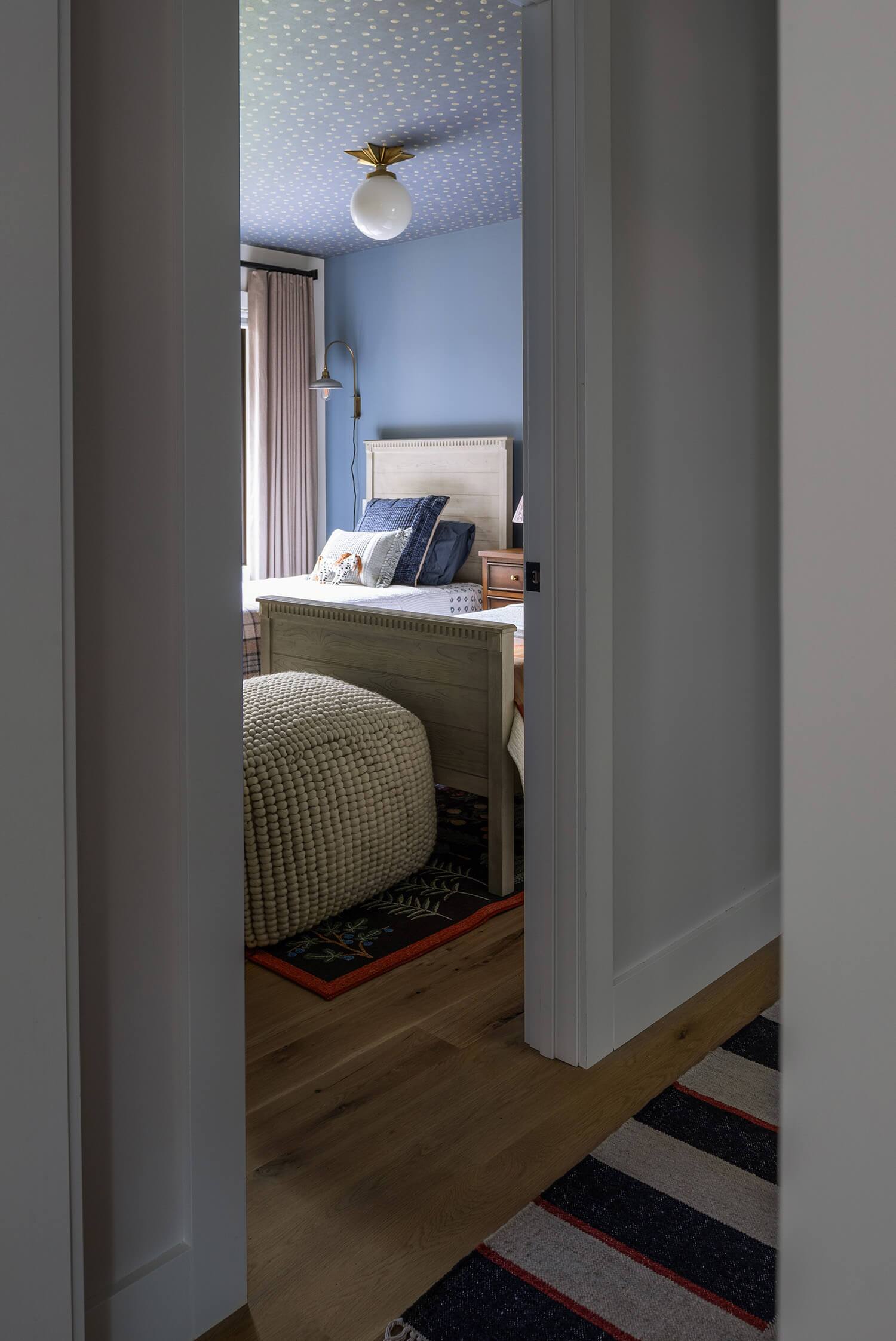 View through doorway into blue kids’ bedroom with patterned ceiling, wooden bed, and cozy layered bedding.