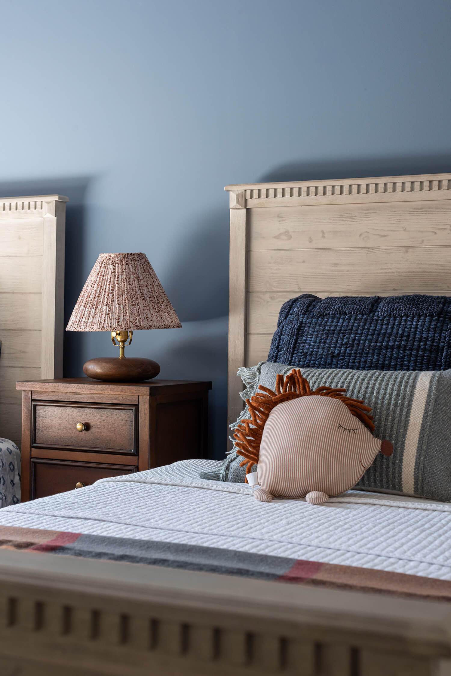 Kids’ bedroom with twin wooden beds, blue walls, playful patterned ceiling, and bedside lamp for warmth.