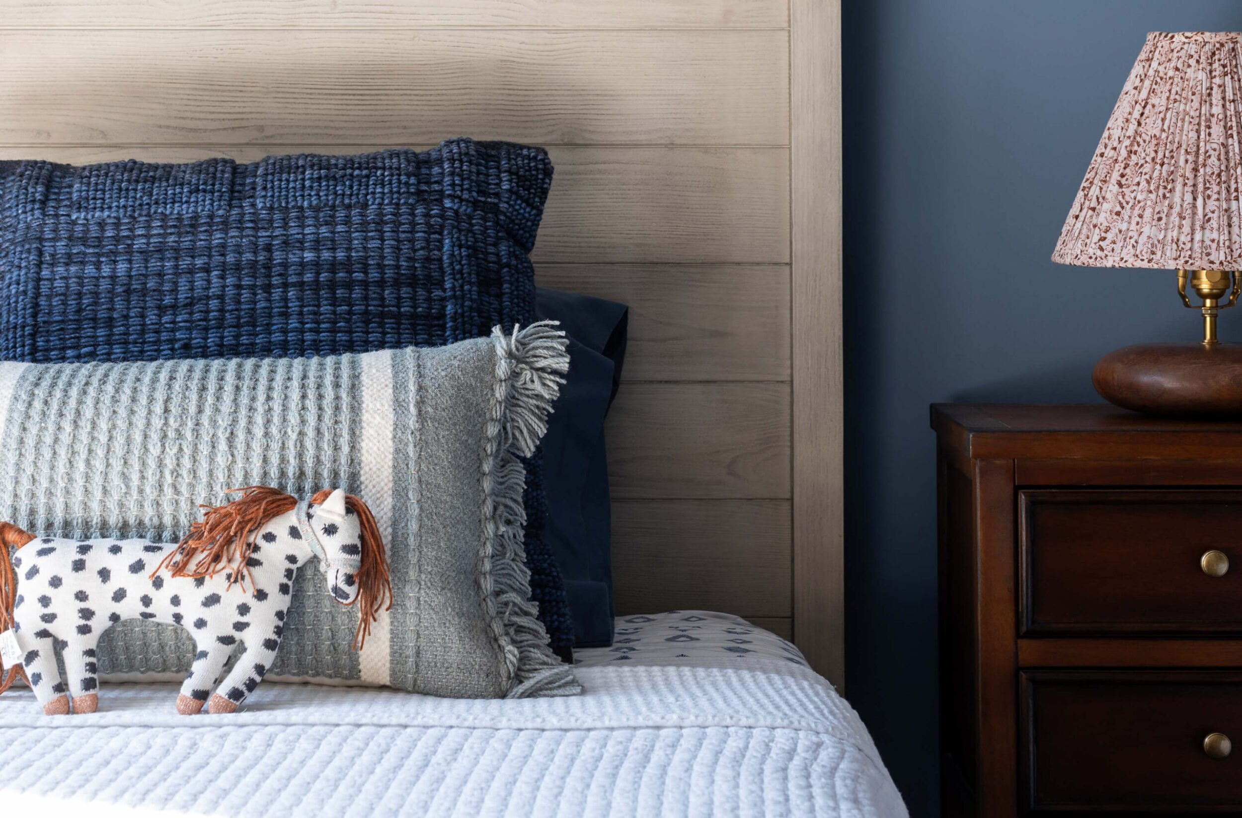 Cozy kids’ bedroom with blue walls, wooden headboards, plush toys, and warm lighting creating a calm, inviting atmosphere.