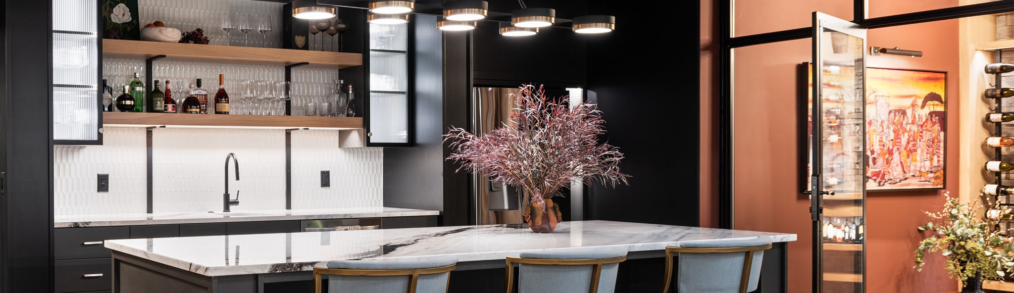 Modern kitchen bar with marble island, open shelving, liquor display, pendant lights, and decorative plant centerpiece