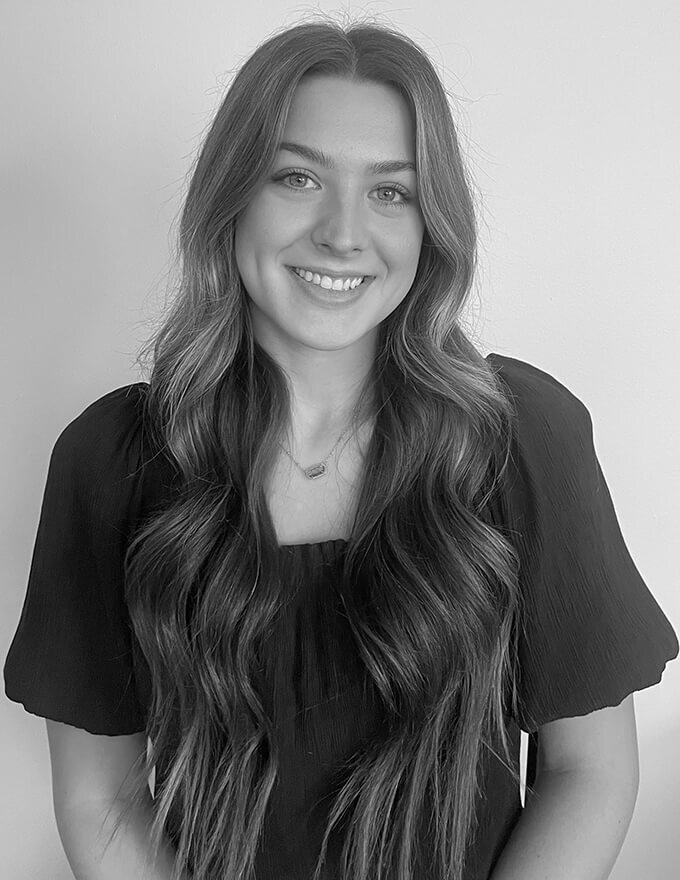 Interior designerin ohio, Young woman with long wavy hair smiles gently at camera, wearing dark blouse; monochrome portrait with soft natural lighting.
