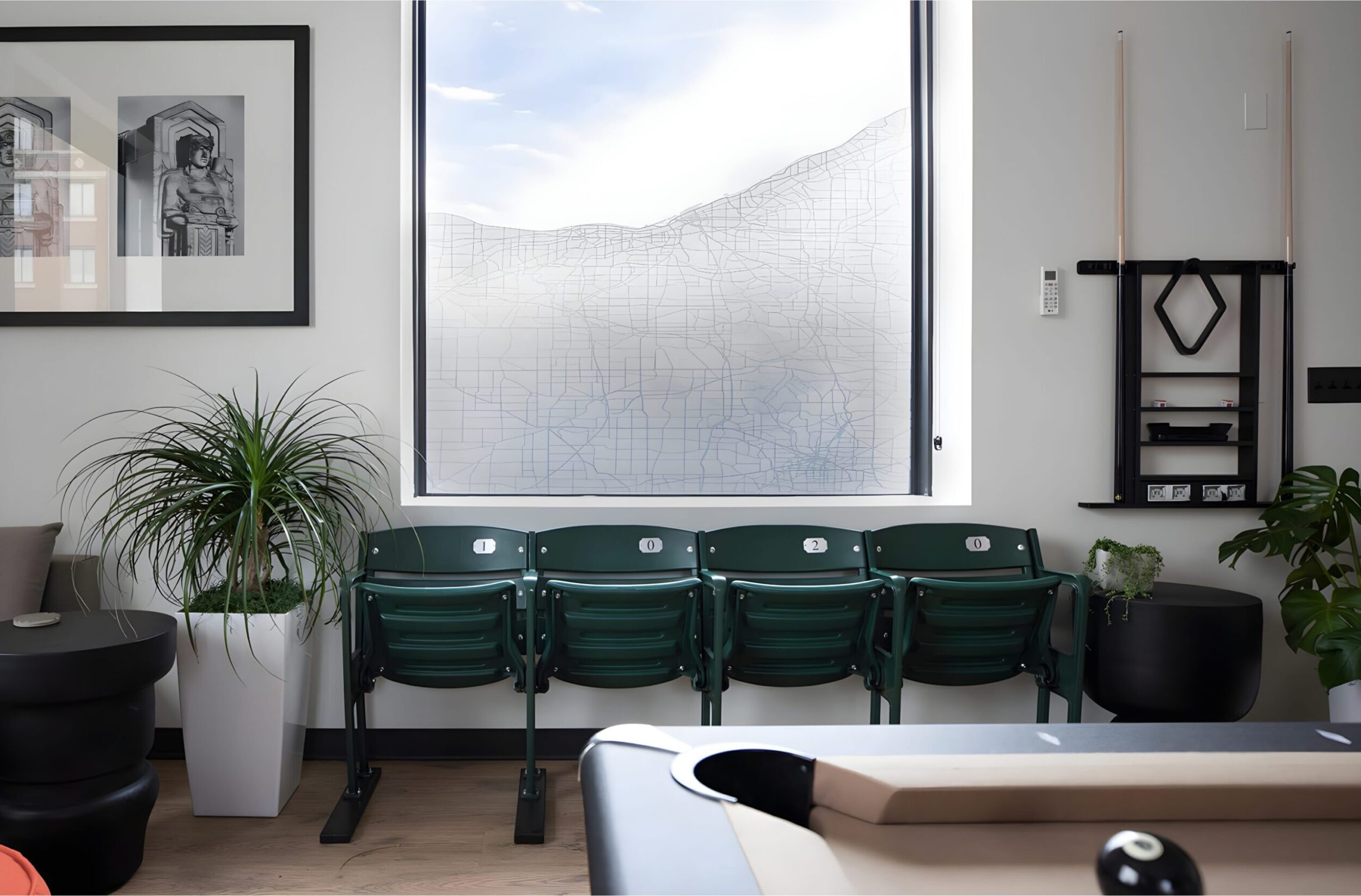 Lounge with green stadium-style chairs, pool table, modern art, and potted plants near large window.