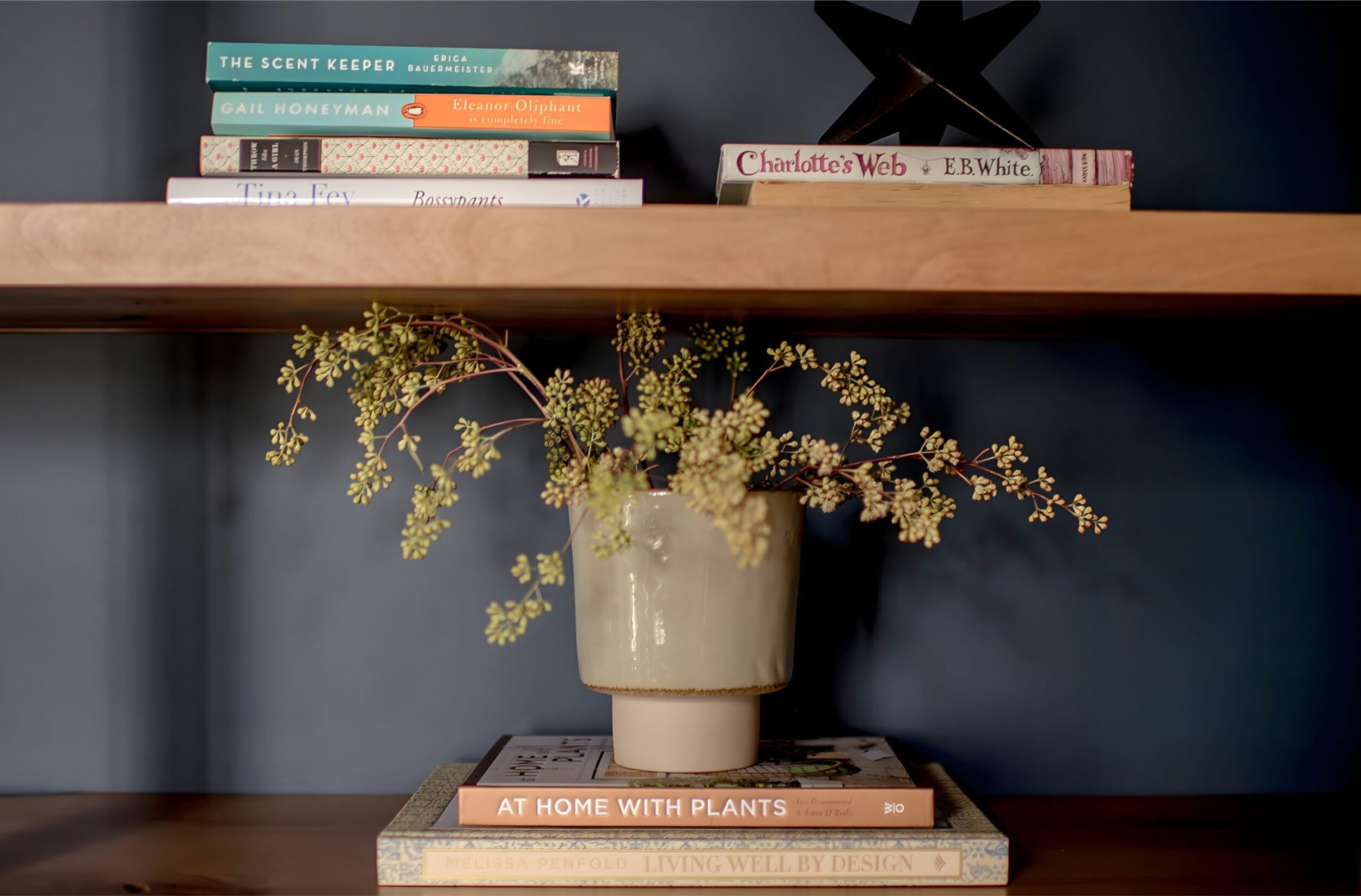 Wooden shelf styled with books and ceramic vase of greenery against dark wall for modern home design.