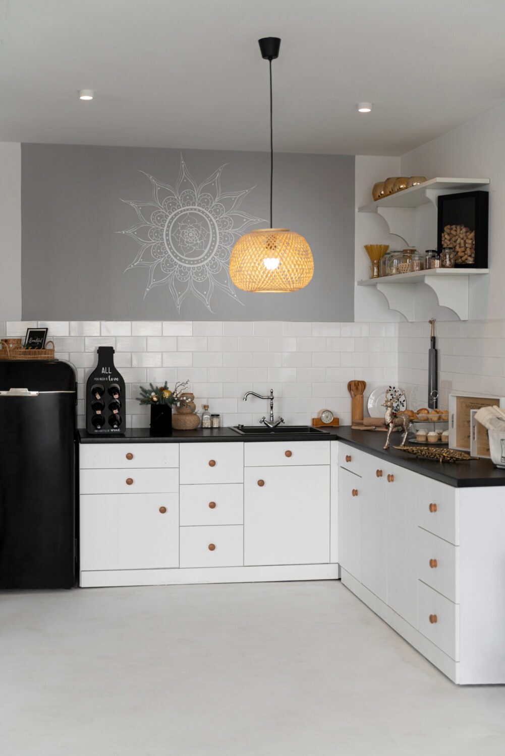 Modern kitchen with white cabinets, black countertop, open shelves, hanging rattan lamp, and decorative wall art.