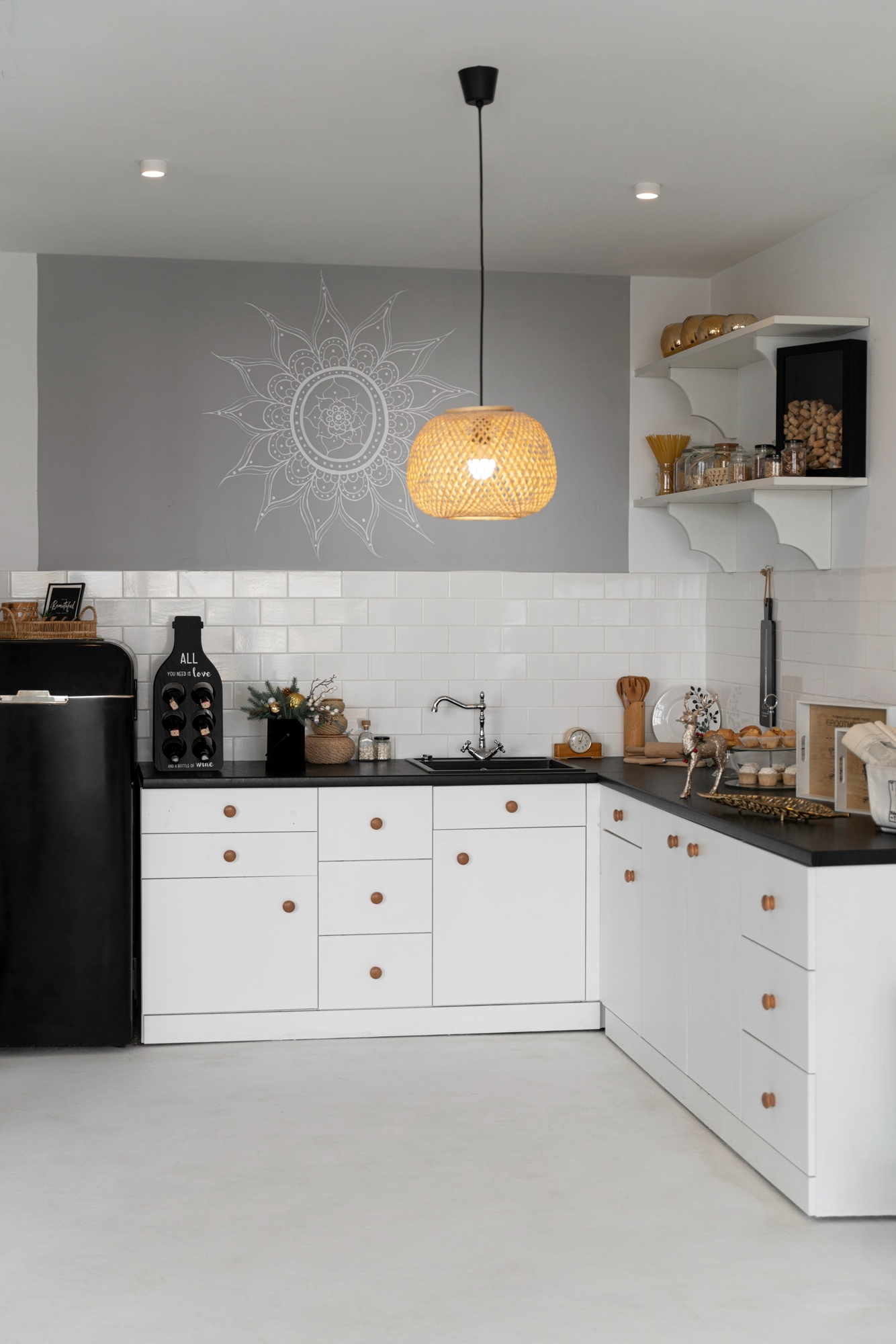 Modern kitchen with white cabinets, black countertop, open shelves, hanging rattan lamp, and decorative wall art.
