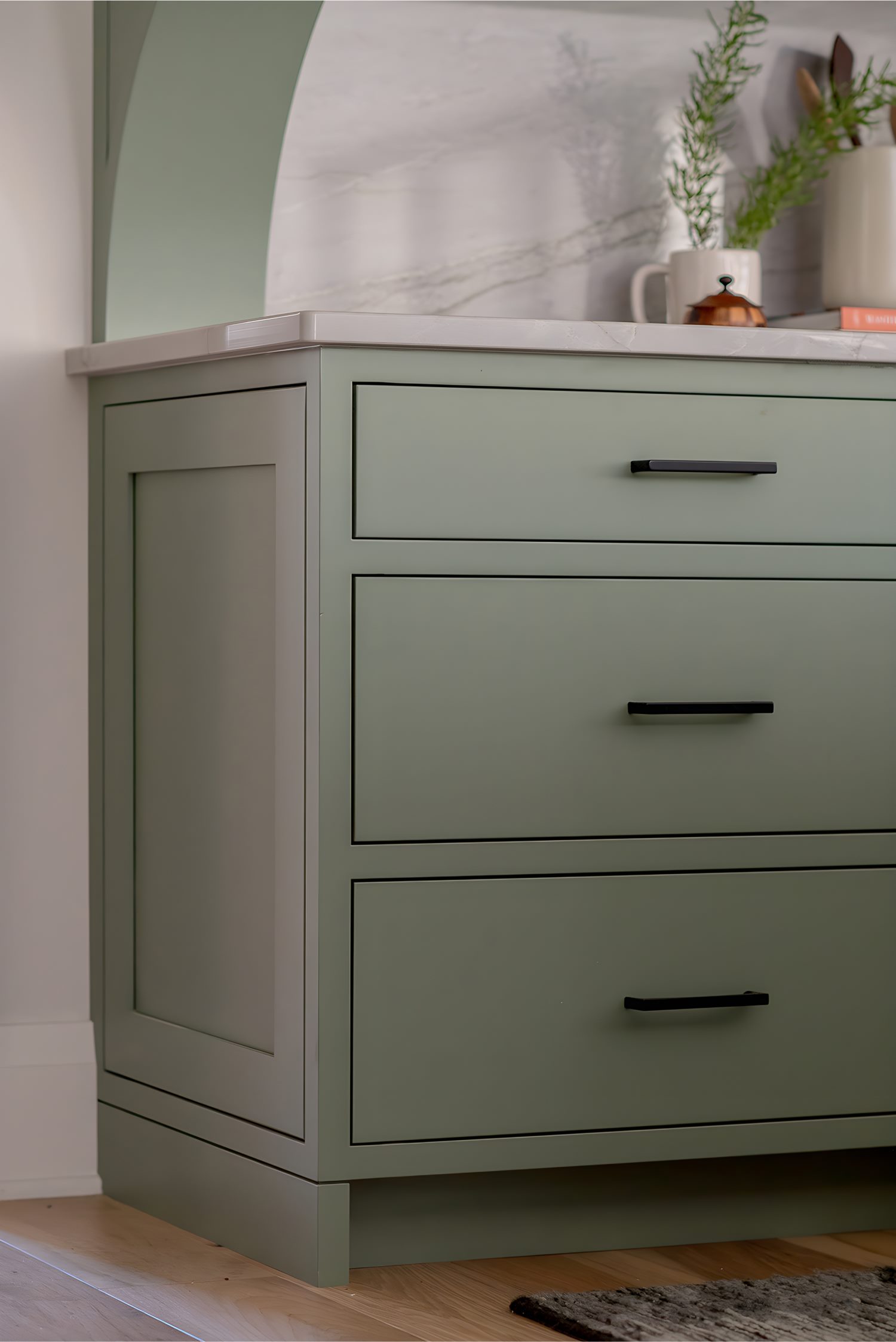 Sage green cabinetry with black handles and marble backsplash detail