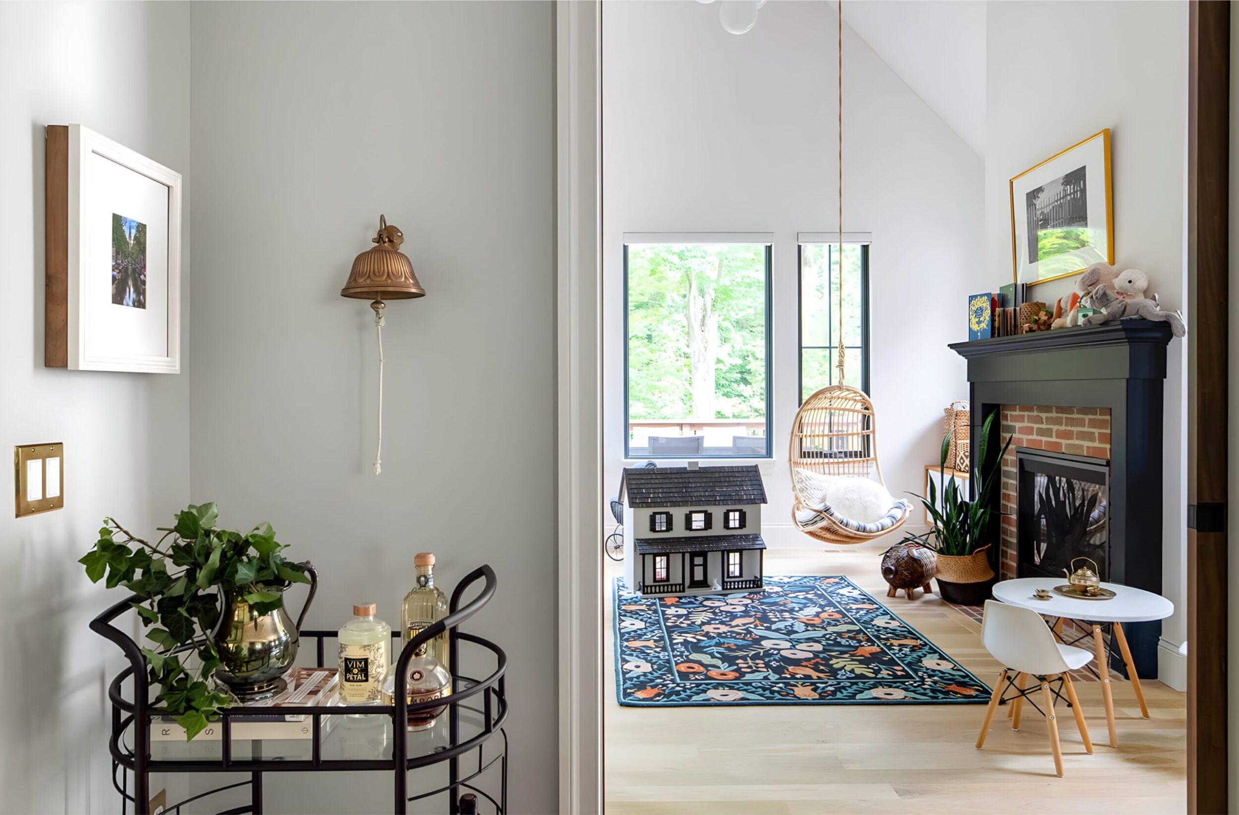 Bright hallway view into playful room with dollhouse, hanging chair, bar cart, and brick fireplace.
