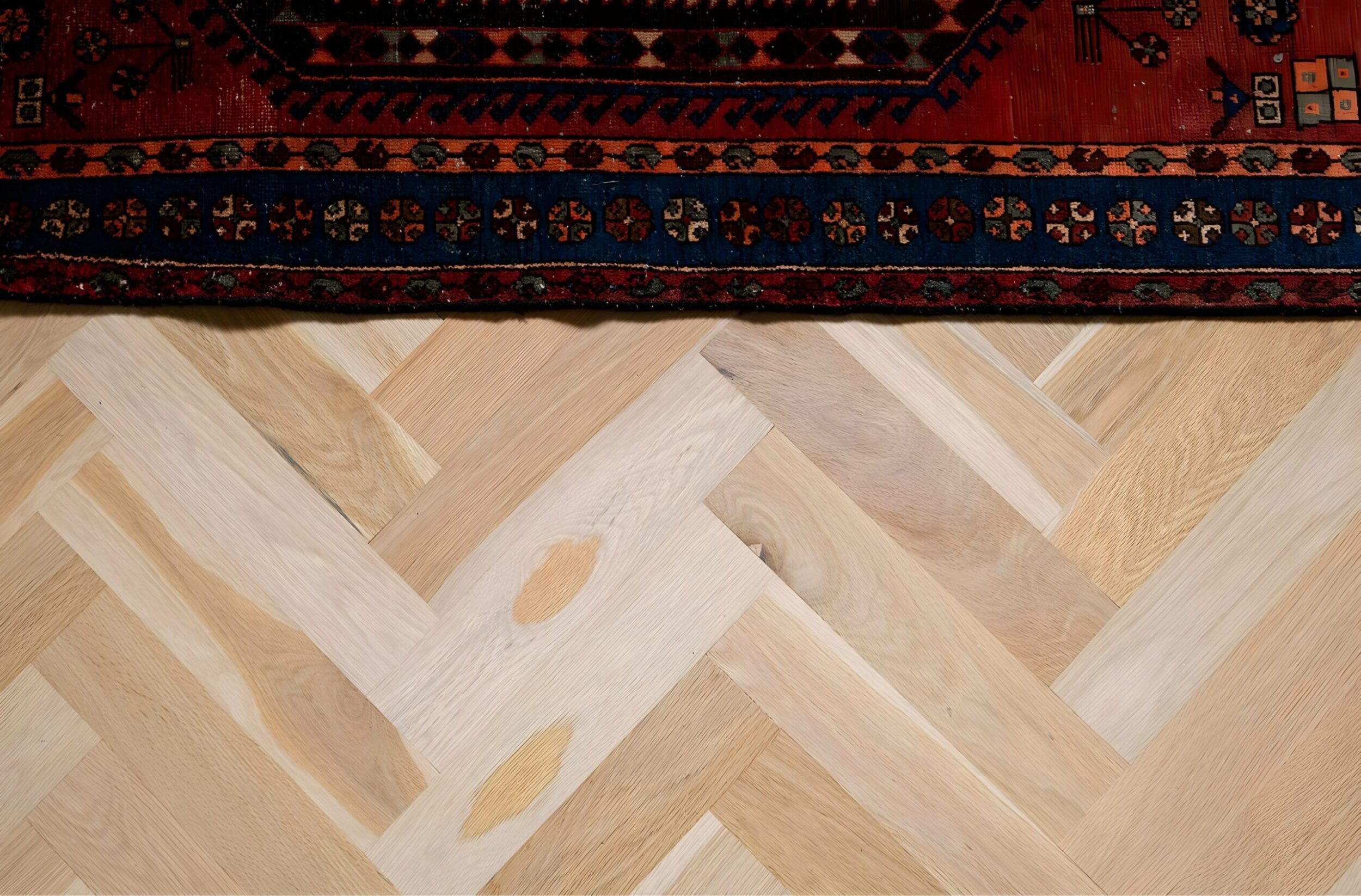 Herringbone wood flooring detail with edge of patterned rug