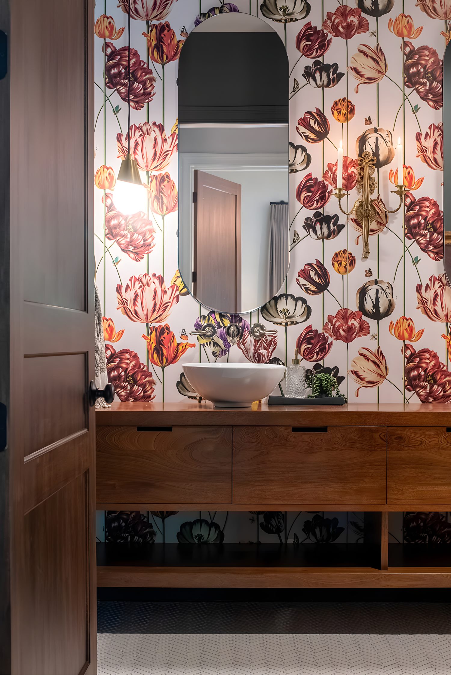 Bold floral wallpapered bathroom with wood vanity, vessel sink, and oval mirror adding dramatic character.