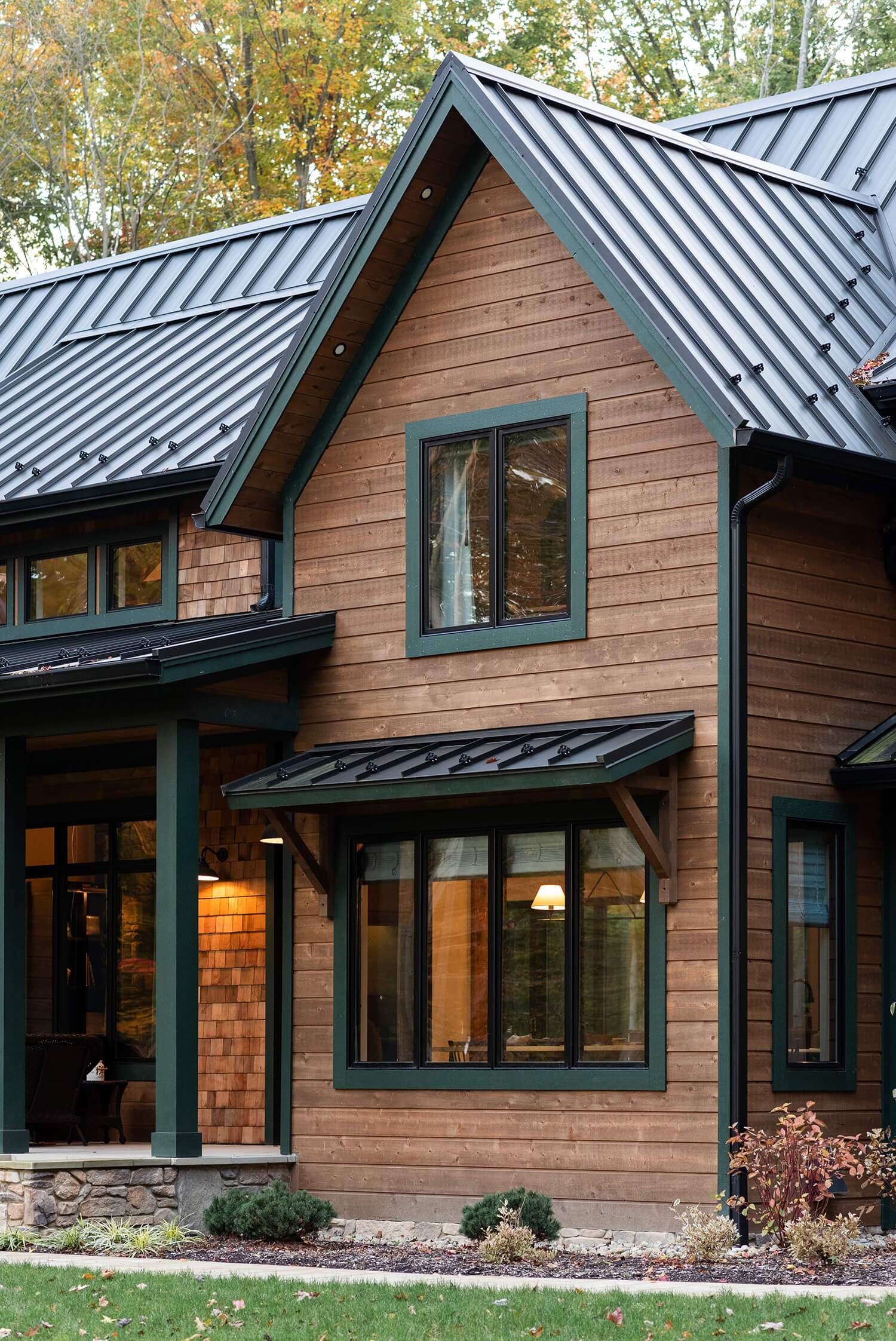 Modern cabin exterior with natural wood siding, dark trim, and metal roof surrounded by autumn trees and greenery