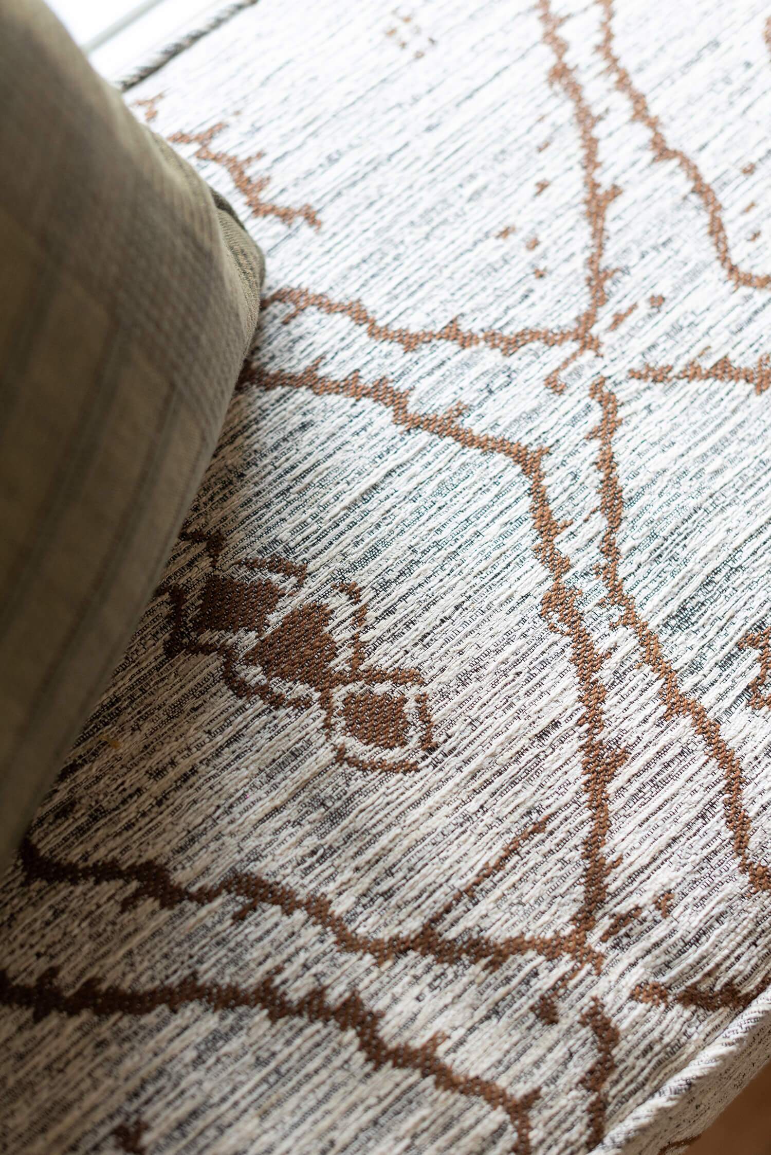 Close-up textured rug detail in soft tones with geometric pattern near cushion, showing warm cozy cabin floor style