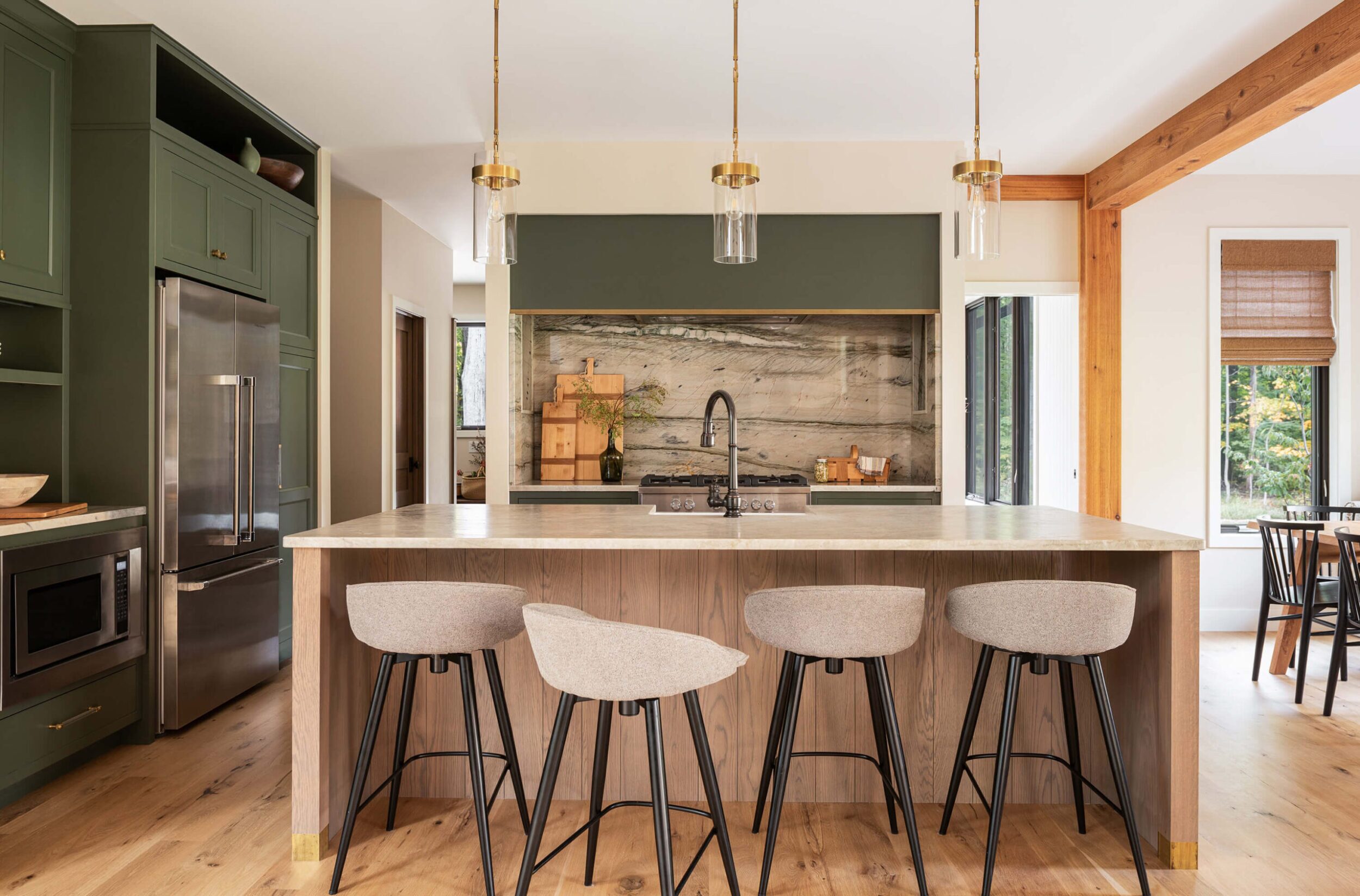 Modern kitchen with marble backsplash, island with stools, green cabinetry, brass pendant lights, and wood accents